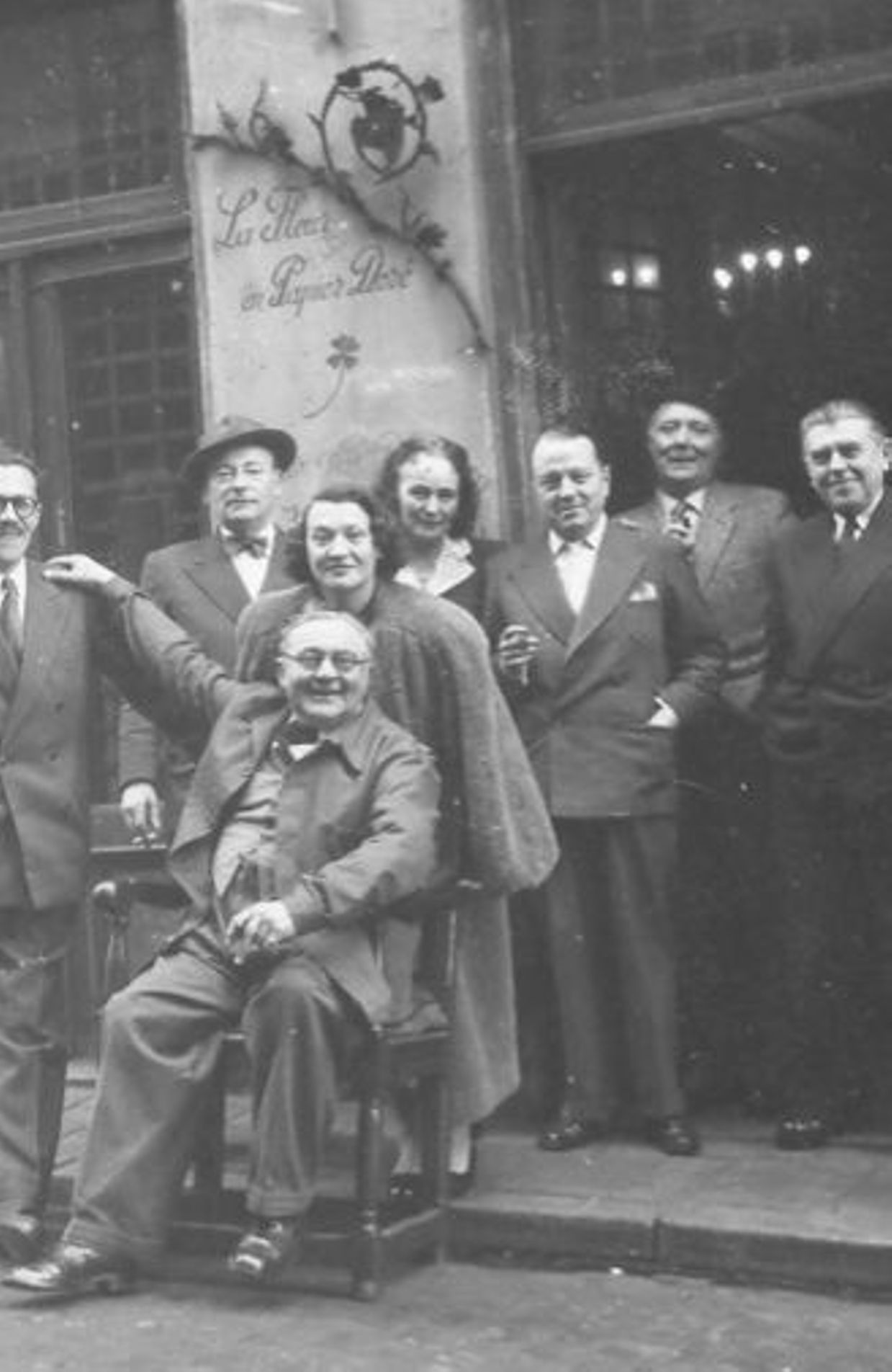 De gauche à droite : Marcel Mariën, Camille Goemans, Gérard Van Bruaene (assis), Irène Hamoir, Georgette Magritte, E.L.T. Mesens, Louis Scutenaire, René Magritte, Paul Colinet, à La Fleur en Papier Doré à Bruxelles