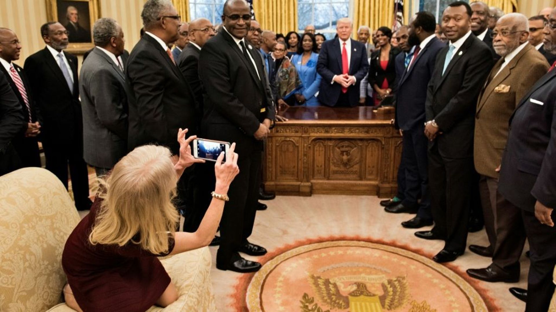 La conseillère du président américain Donald Trump, Kellyanne Conway (g), agenouillée sur un sofa pour prendre une photo du président avec des dirigeants de lycées et d'universités historiquement noirs, le 27 février 2017 dans le Bureau Ovale de la Maison
