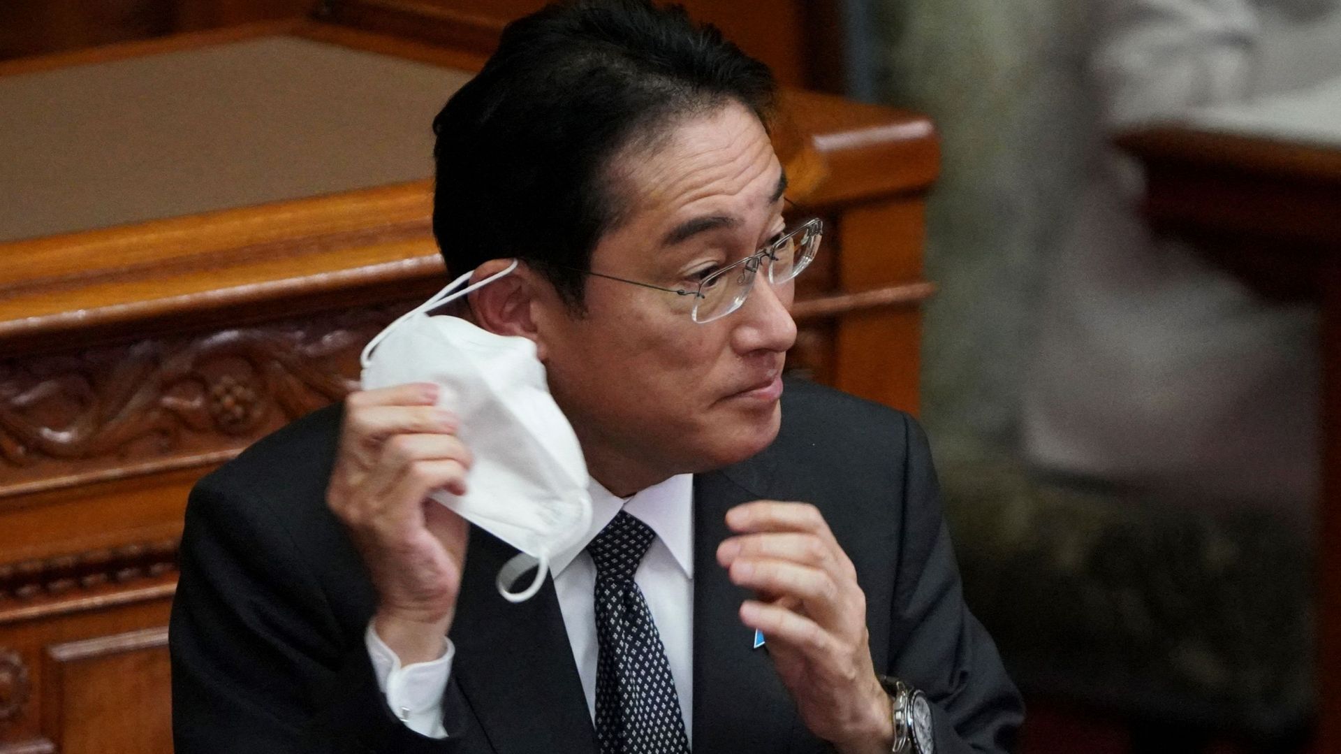 Le Premier ministre japonais Fumio Kishida enlève son masque facial avant son discours lors d'une session plénière de la chambre haute du parlement à Tokyo, le 27 janvier 2023