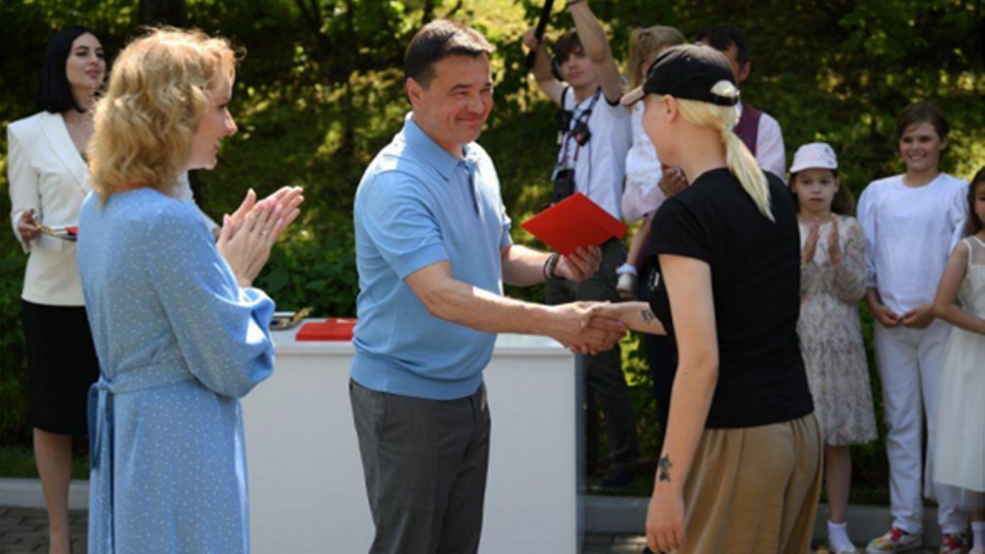 Juillet 2022. Maria Lvova-Belova regarde une adolescente du Donbass recevoir son passeport russe des mains d’Andrey Vorobyov, gouverneur de l’Oblast de Moscou, lors de la cérémonie de naturalisation.