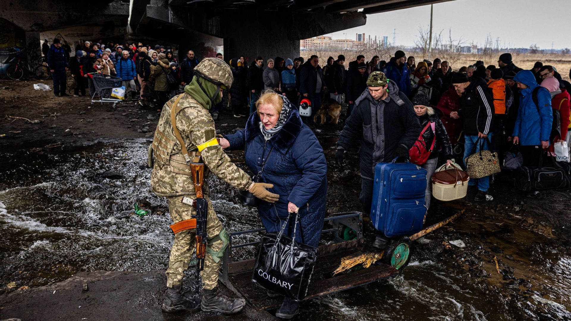 Un militaire ukrainien aide des personnes rassemblées sous un pont détruit, alors qu'elles fuient la ville d'Irpin, au nord-ouest de Kiev.