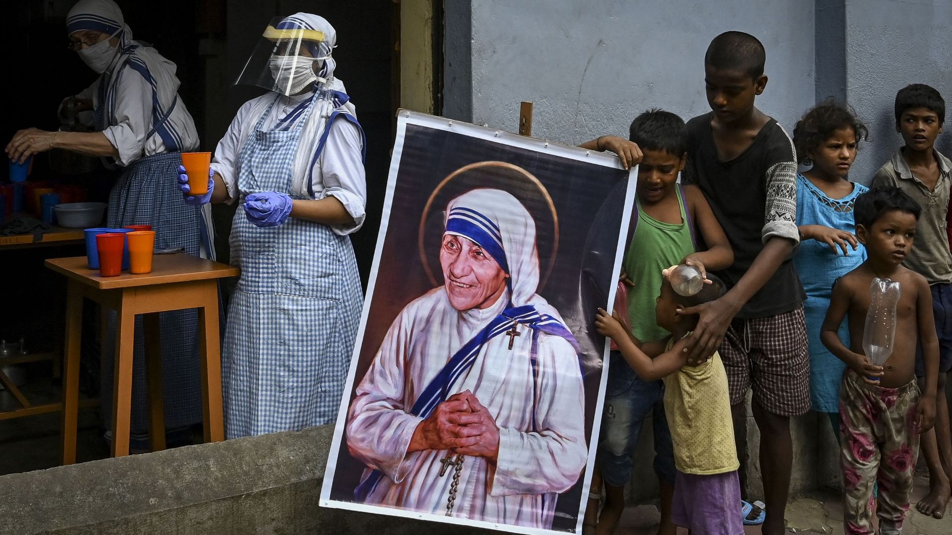 Des sœurs des Missionnaires de la charité distribuent de la nourriture à Calcutta, devant un portrait de Mère Teresa.