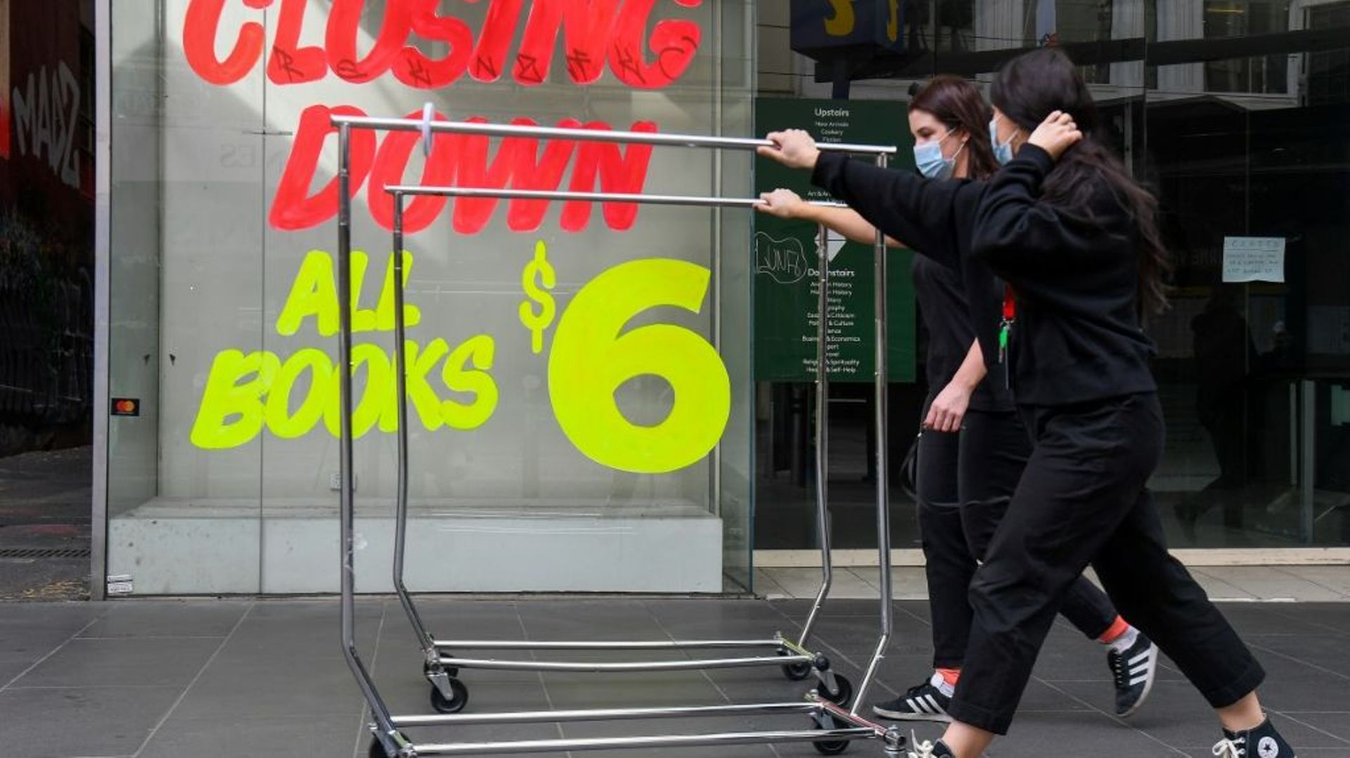 Des employées poussent des portants devant une boutique fermée, le 3 août 2020 à Melbourne, en Australie, après l'annonce de nouvelles restrictions pour lutter contre la pandémie de coronavirus