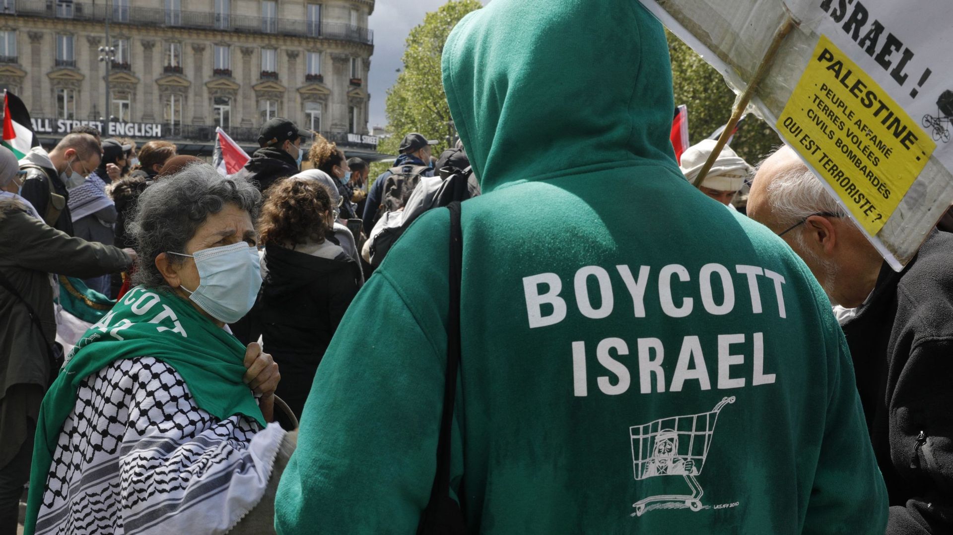 Un homme porte un sweat à capuche sur lequel on peut lire "Boycott Israël" alors que des manifestants crient des slogans et agitent des drapeaux palestiniens lors d’une manifestation de solidarité avec le peuple palestinien sur la place de la République à