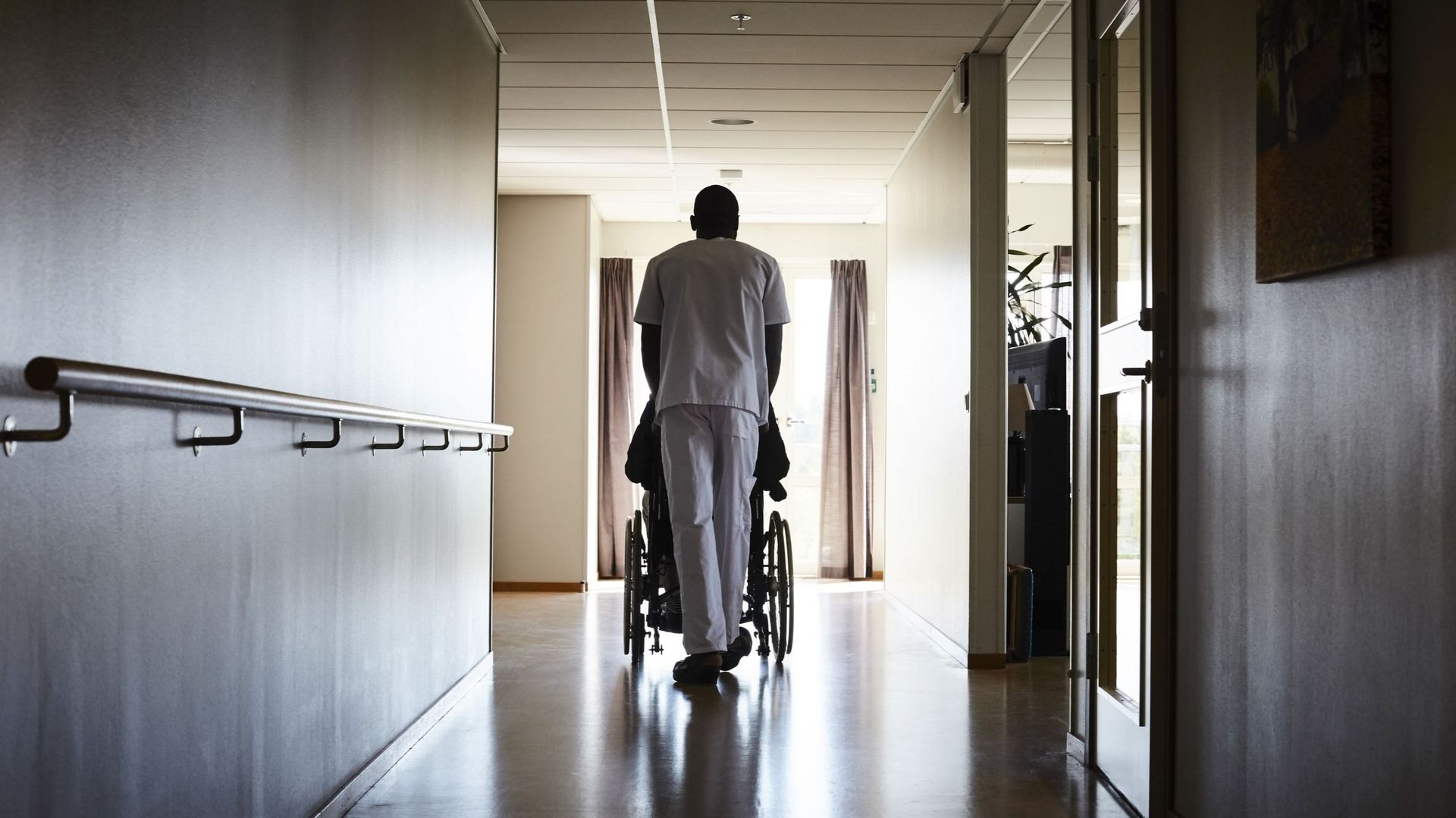 Full length rear view of male nurse pushing senior man on wheelchair at hospital corridor