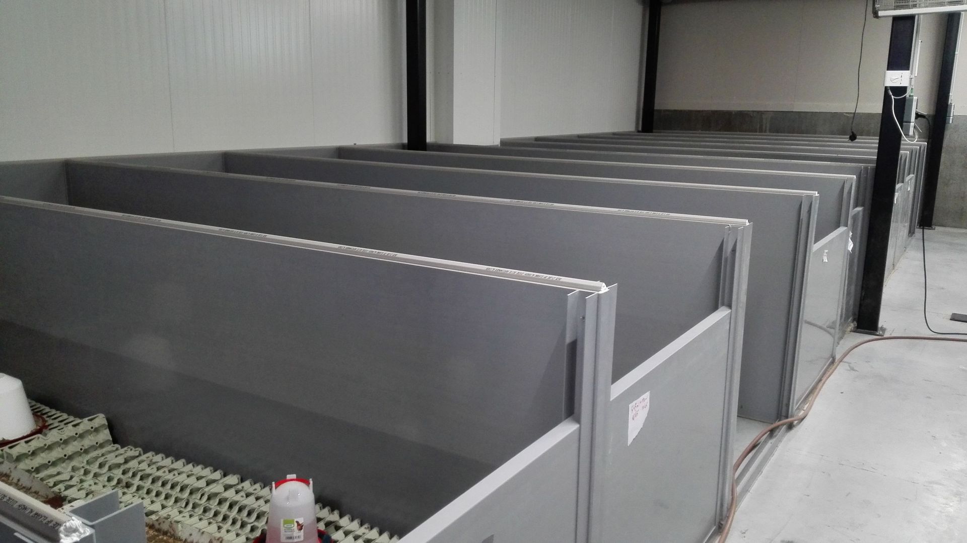 Une dizaine de boxes en plastique gris sont alignés de part et d'autre d'une allée centrale, à l’intérieur, des millions de grillons. 