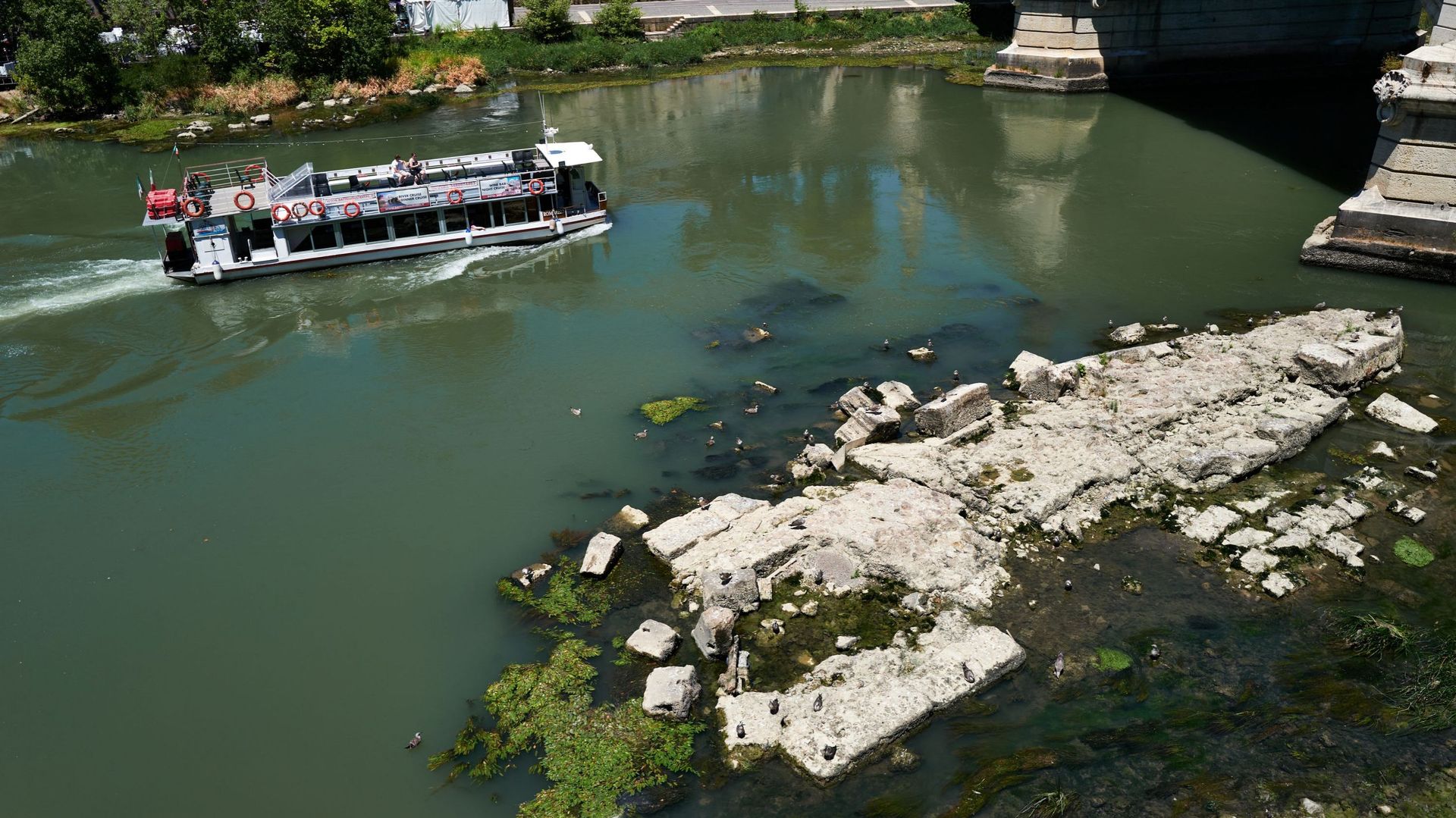 Cette photo prise le 2 juillet 2022 à Rome montre un bateau fluvial touristique naviguant près du pont Vittorio Emanuele II, alors que le faible niveau d’eau du Tibre révèle un ancien pont construit sous l’empereur romain Néron (en bas à droite). Andreas 