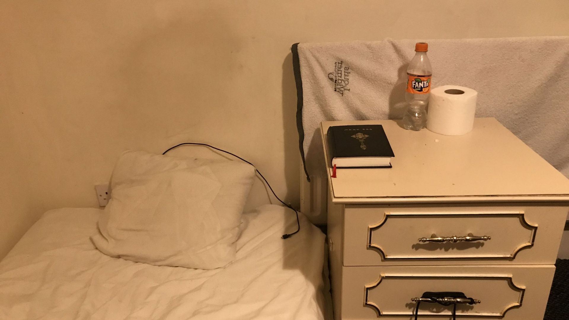 Dans sa chambre, un matelas posé à terre, une table de nuit avec la Bible 