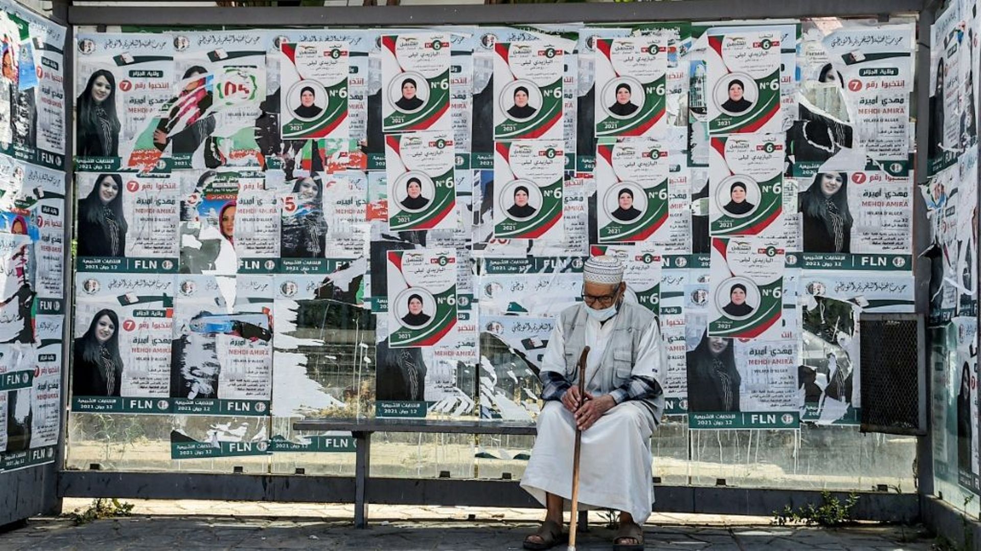 Un vieil homme attend à une station de bus recouverte d'affiches électorales, le 11 juin 2021 à Alger, à la veille des législatives