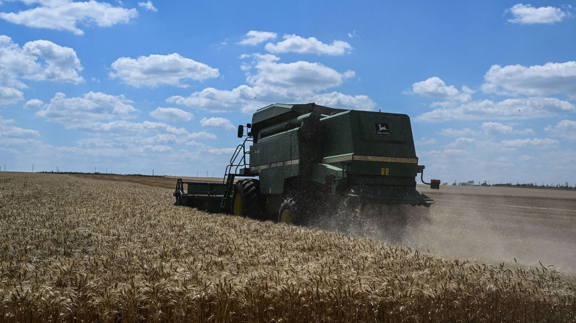 Une photo prise le 15 juillet 2022 montre une plantation de blé avec une moissonneuse-batteuse en arrière-plan près de Kramatorsk, dans l'Oblast de Donetsk, dans l'est de l'Ukraine, en pleine invasion russe de l'Ukraine.