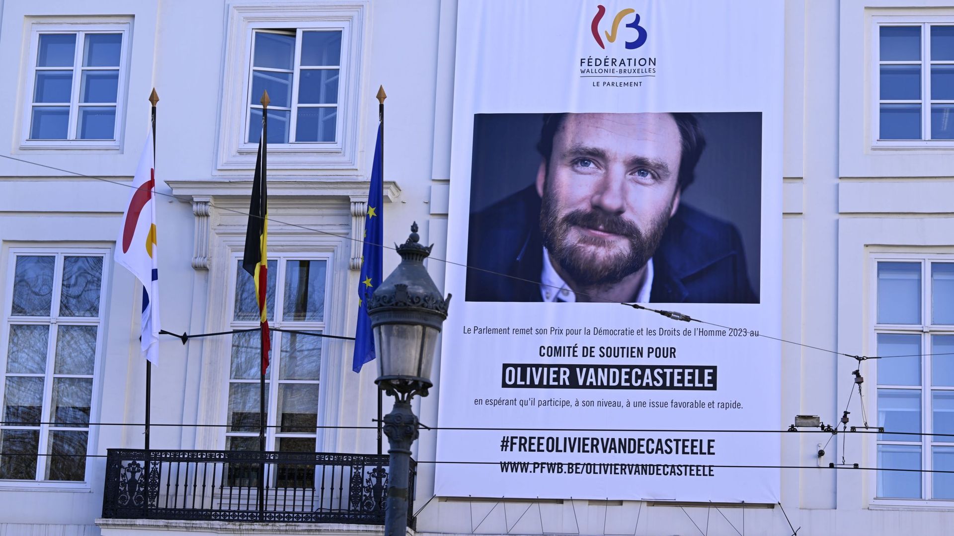 L’illustration montre une grande banderole en faveur du travailleur humanitaire Olivier Vandecasteele, emprisonné en Iran, à l’extérieur, lors d’une session plénière du Parlement de la Fédération Wallonie-Bruxelles.