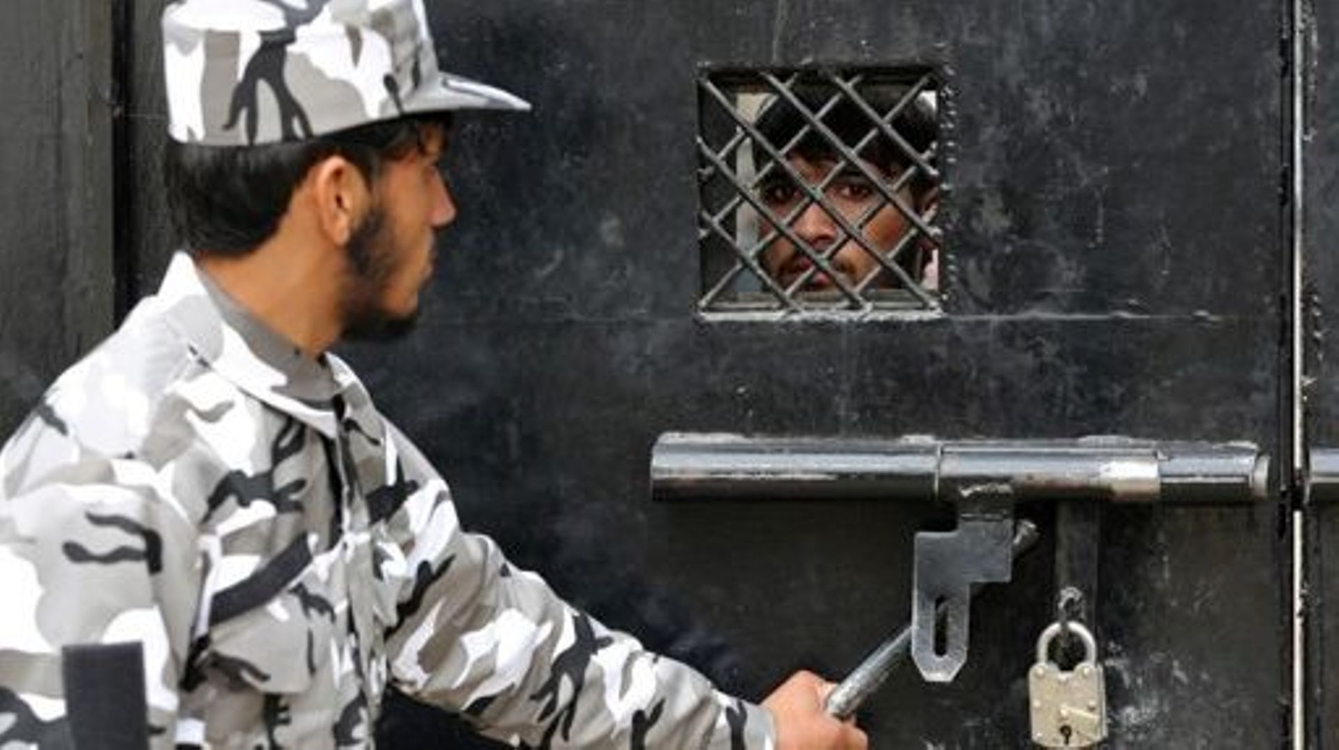 A member of Taliban security force stands guard as an inmate watches from behind the closed gate of a prison in Jalalabad on January 19, 2023.  Shafiullah KAKAR / AFP
