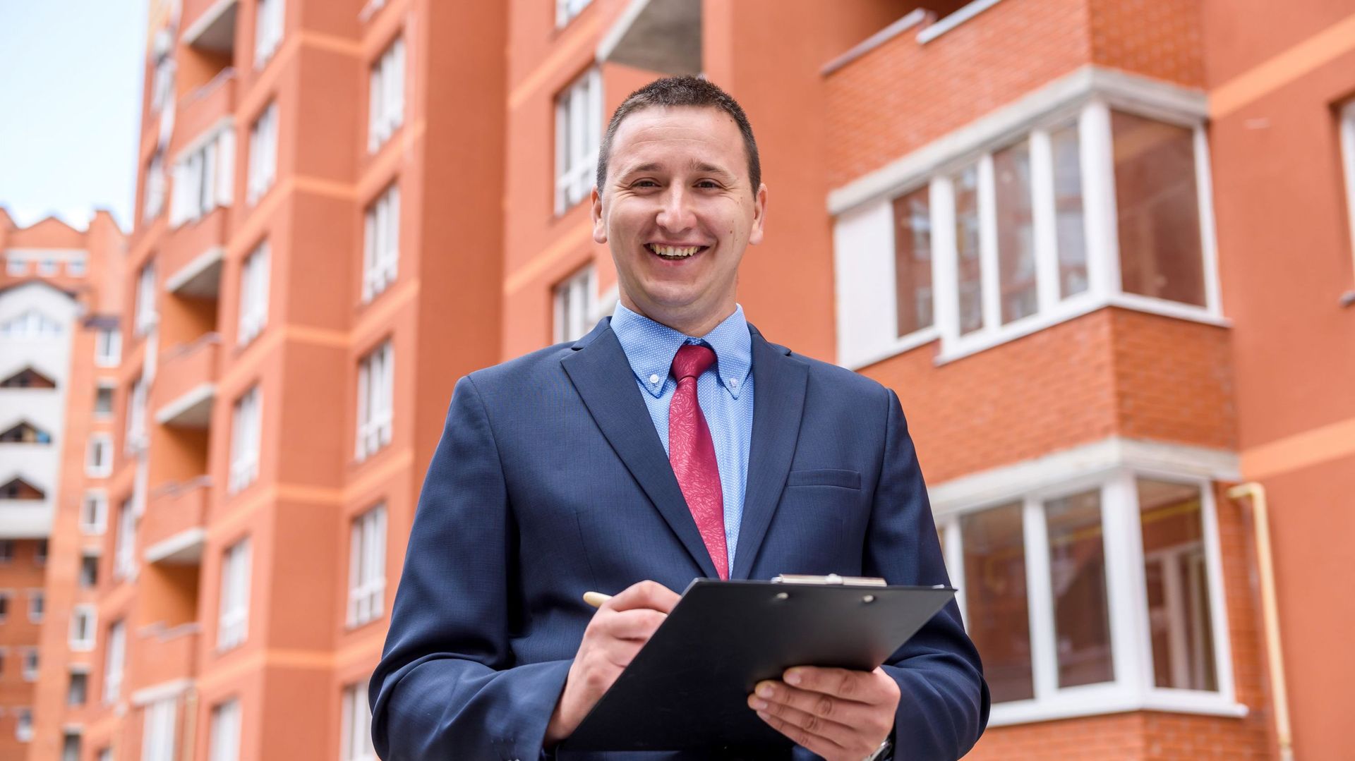 Agent posing with clipboard against new house