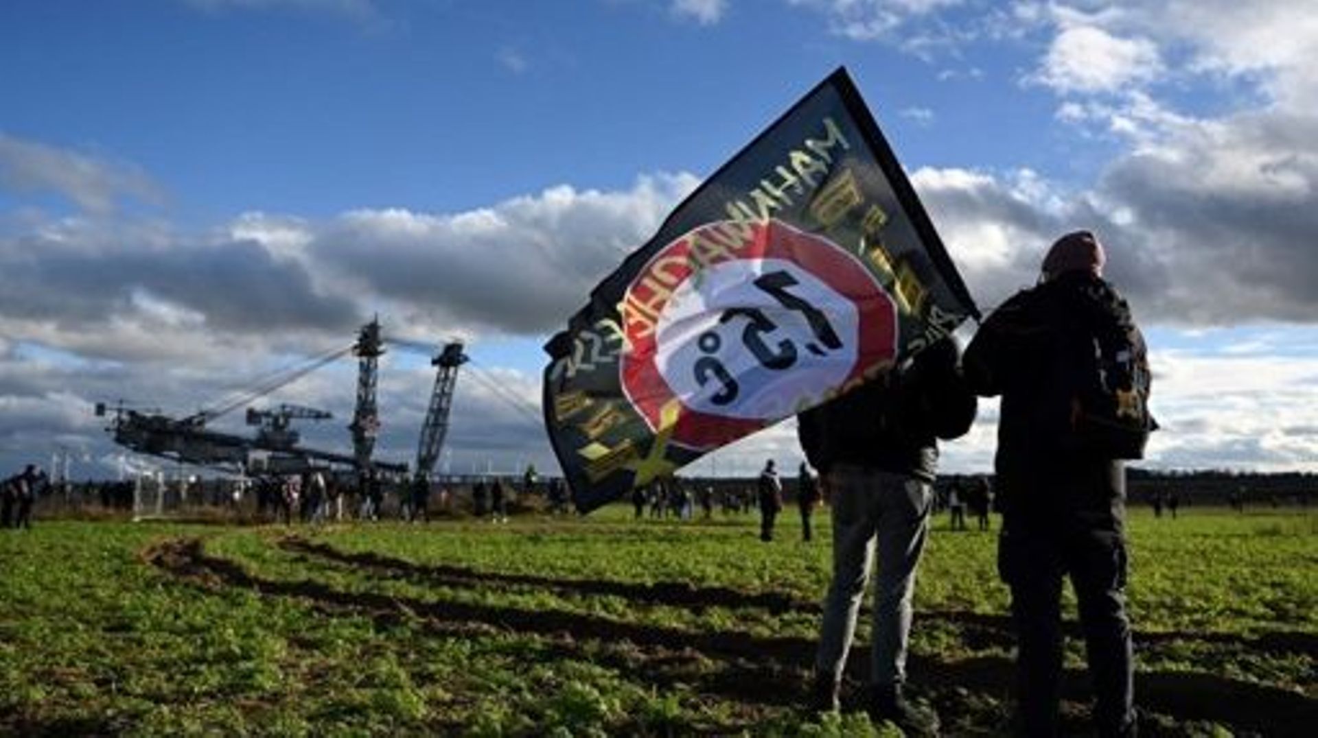 Activists stand with a flag with the lettering '1,5 degrees Celsius' at the Garzweiler lignite open cast mine ahead of the imminent clearance of the nearby village of Luetzerath, western Germany on January 8, 2023. Police prepare the planned evacuation o