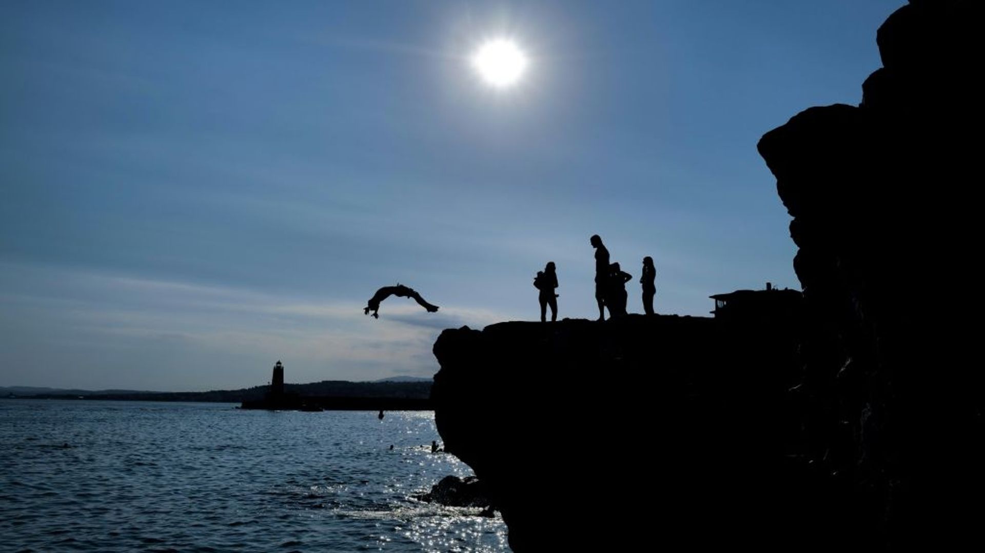 Des nageurs sautent d'un rocher dans la mer Méditerranée, à Nice dans les Alpes-Maritimes, le 10 juillet 2022
