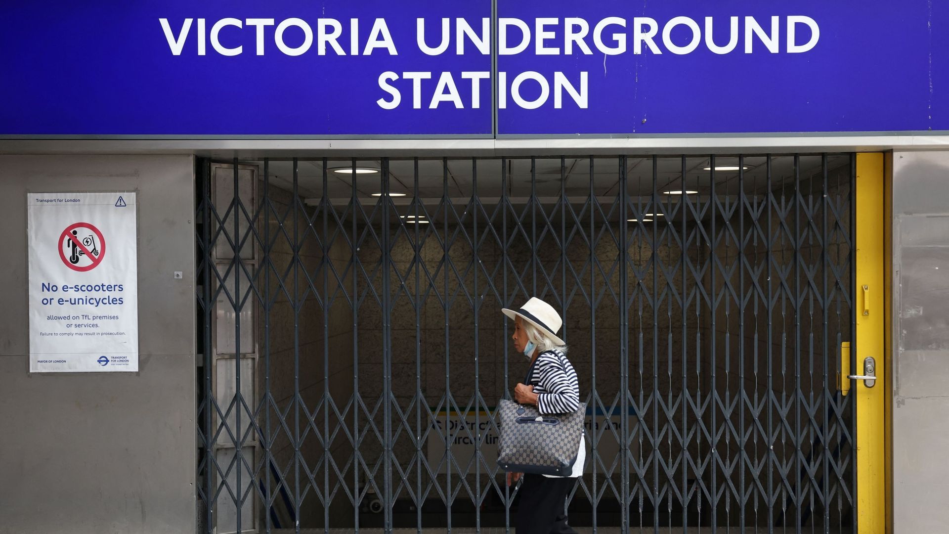 Une piétone passe devant les portes fermées de la station de métro Victoria, à Londres, le 19 août 2022, alors que la grève des bus, des chemins de fer nationaux et du métro londonien affecte les services.