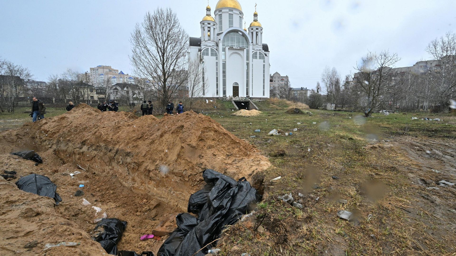 Une fosse commune est vue derrière une église dans la ville de Bucha, au nord-ouest de la capitale ukrainienne Kiev, le 3 avril 2022. Le maire de la ville, Anatoly Fedoruk, a déclaré à l’AFP que 280 autres corps avaient été enterrés dans des fosses commun