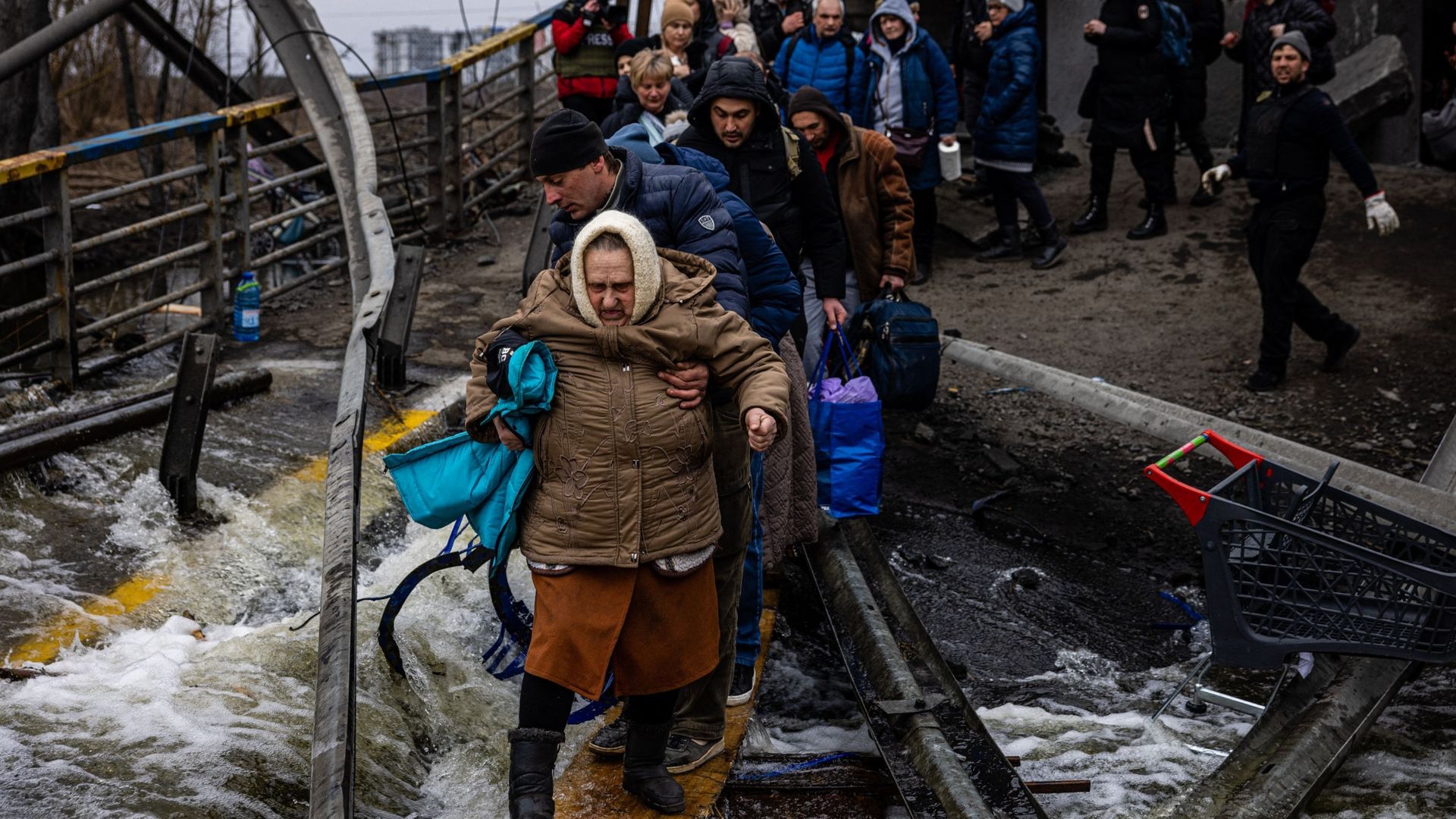 Un homme aide une femme évacuée à traverser un pont détruit alors qu’elle et d’autres personnes fuient la ville d’Irpin, au nord-ouest de Kiev, le 7 mars 2022.