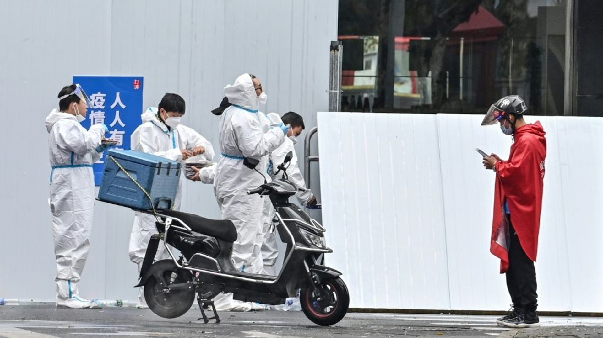 Un livreur (d) près d’employés en combinaison de protection devant un quartier confiné de Shanghai après l’apparition de nouveaux cas de Covid-19, le 17 mars 2022 en Chine