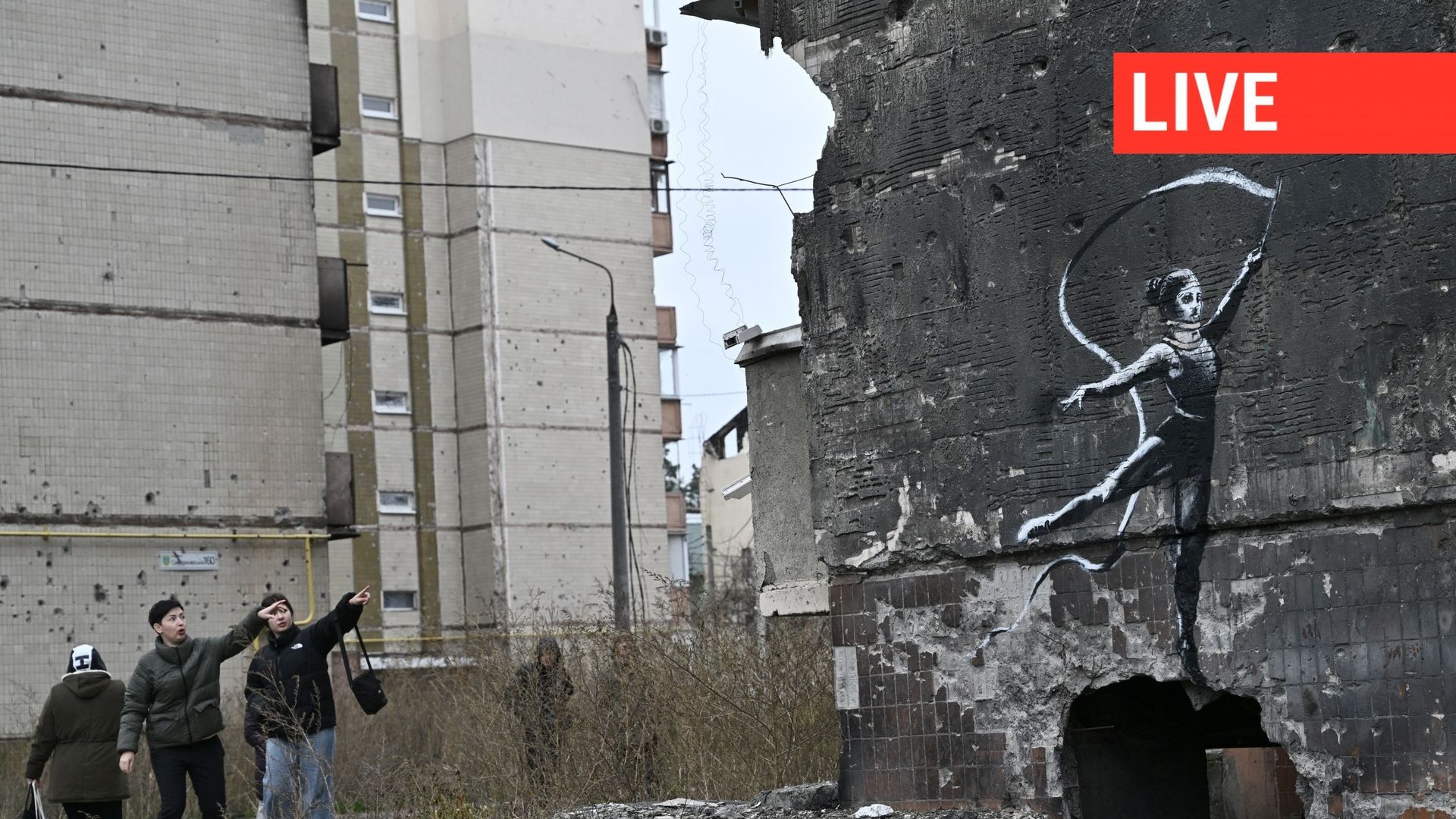 Des résidents d’Irpin, près de Kiev, observent un graffiti de style Banksy sur le mur d’un immeuble résidentiel détruit, mais dont l’origine n’est pas confirmée par l’artiste le 12 novembre 2022, en pleine invasion de l’Ukraine par la Russie. Banksy, l’in