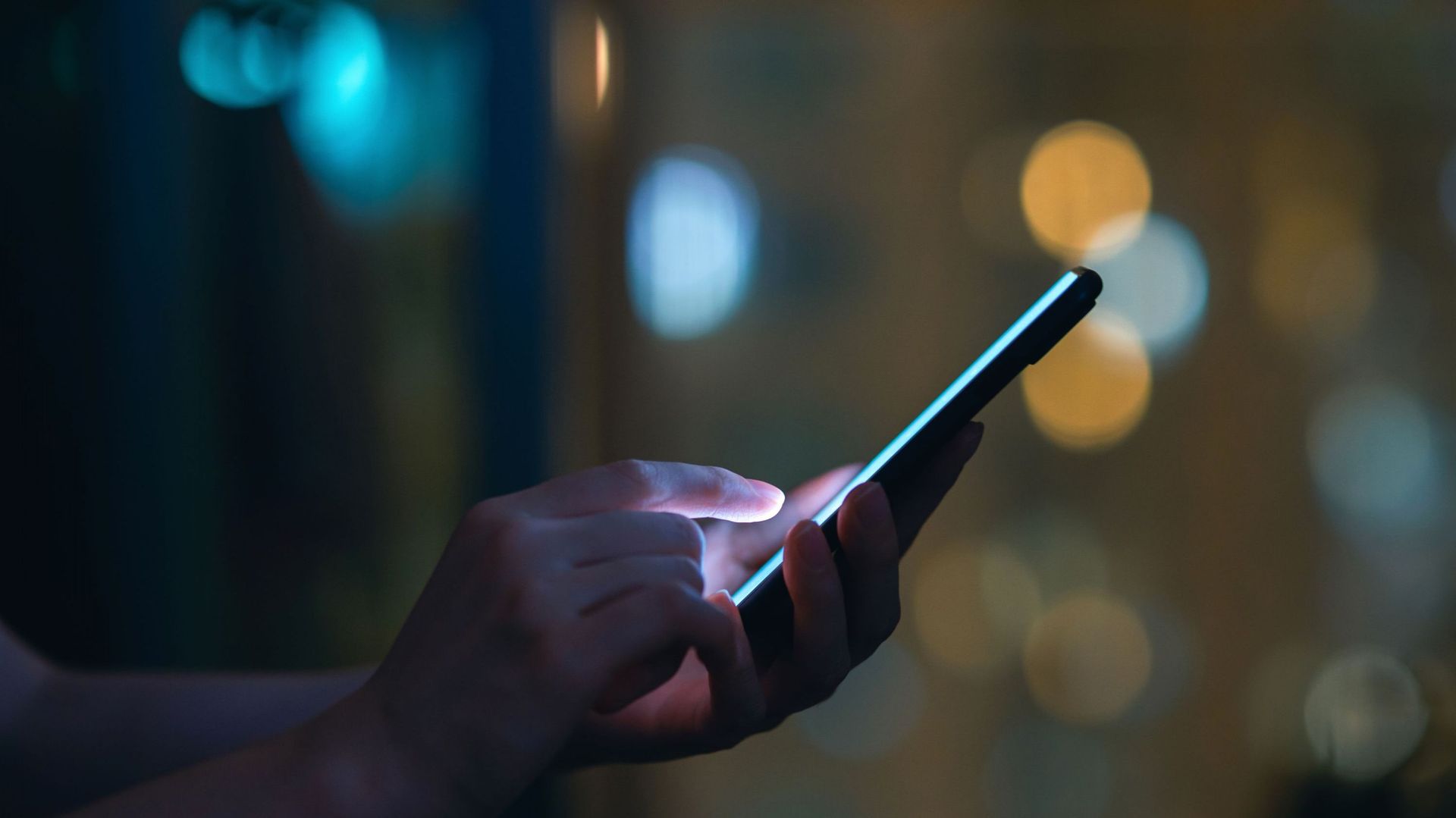 Close up of woman&#39;s hand using smartphone in the dark, against illuminated city light bokeh