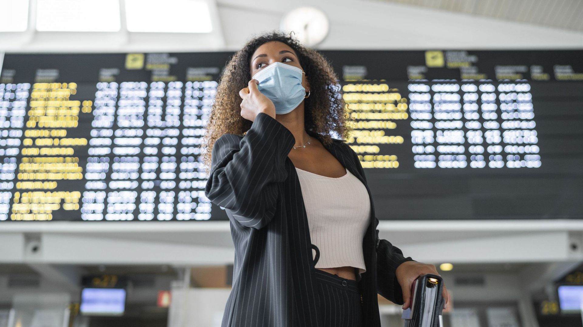 Woman wearing protective face mask talking on smart phone at airport