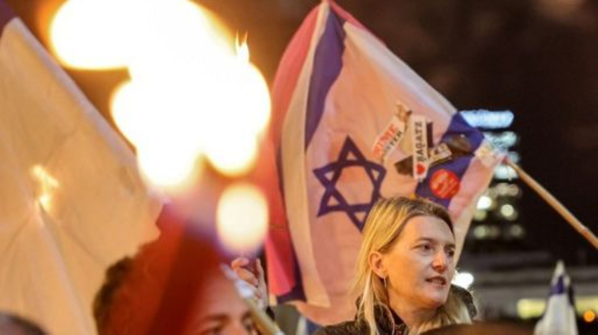 Un manifestant marche avec une torche et d’autres avec des drapeaux nationaux israéliens lors d’une manifestation contre le projet de réforme judiciaire controversé du gouvernement à Tel Aviv le 9 mars 2023. JACK GUEZ / AFP