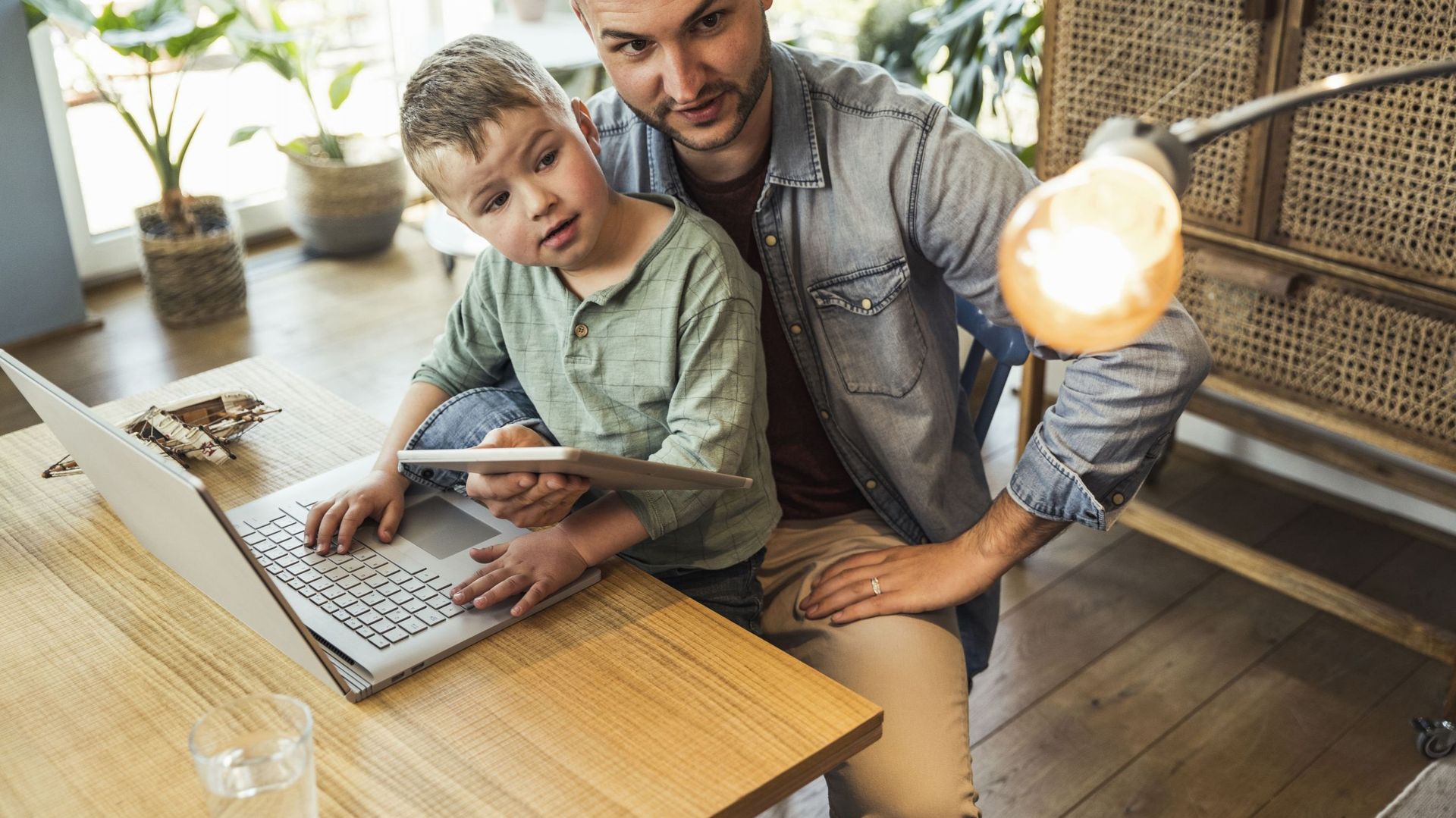 Man and child looking at burning lightbulb controlled by using tablet