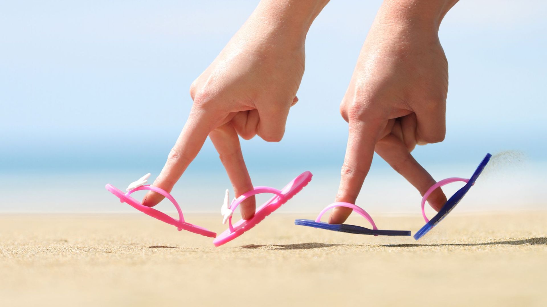 Two hands with flip flops on fingers on beach
