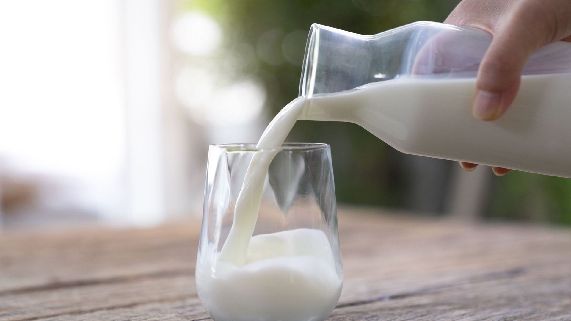 The milk is poured into a ceramic jug into a glass on a natural background.