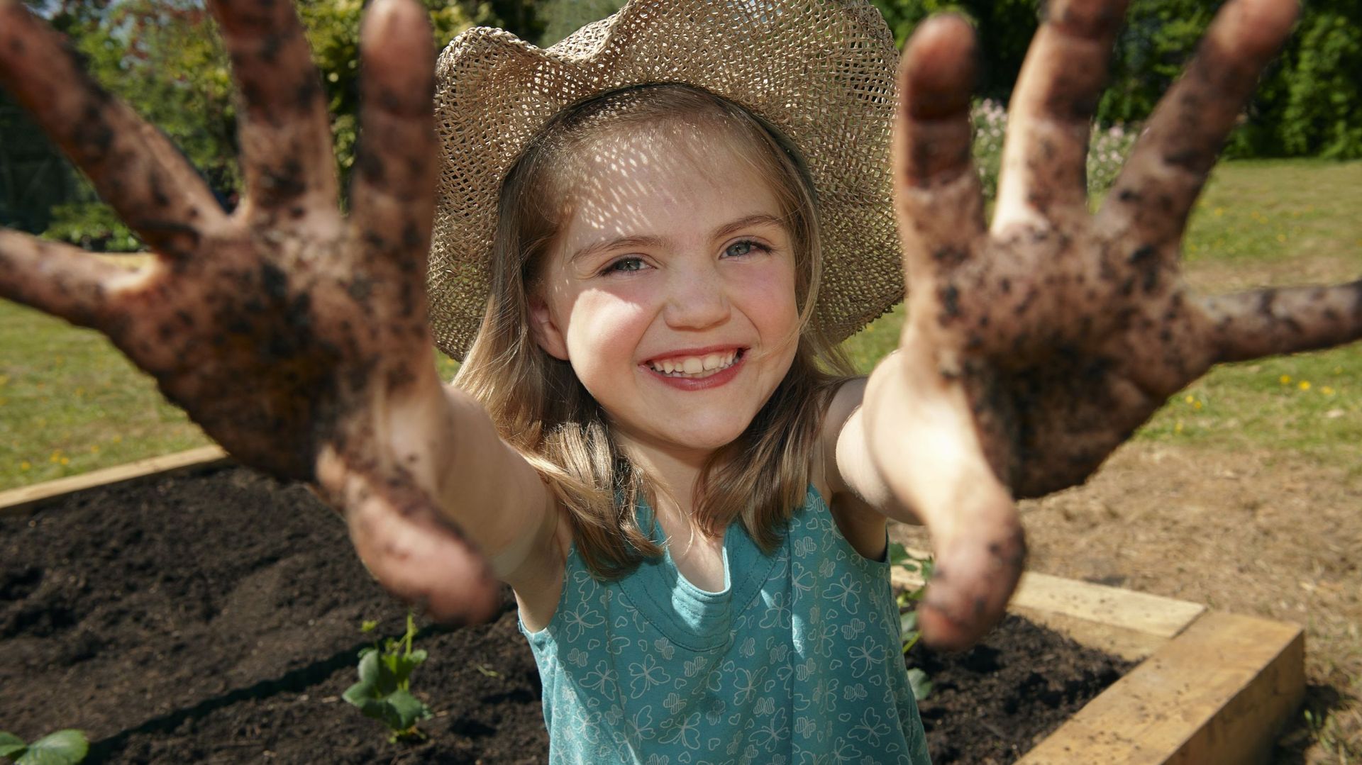 Une petite fille qui jardine montre ses mains pleines de terre.