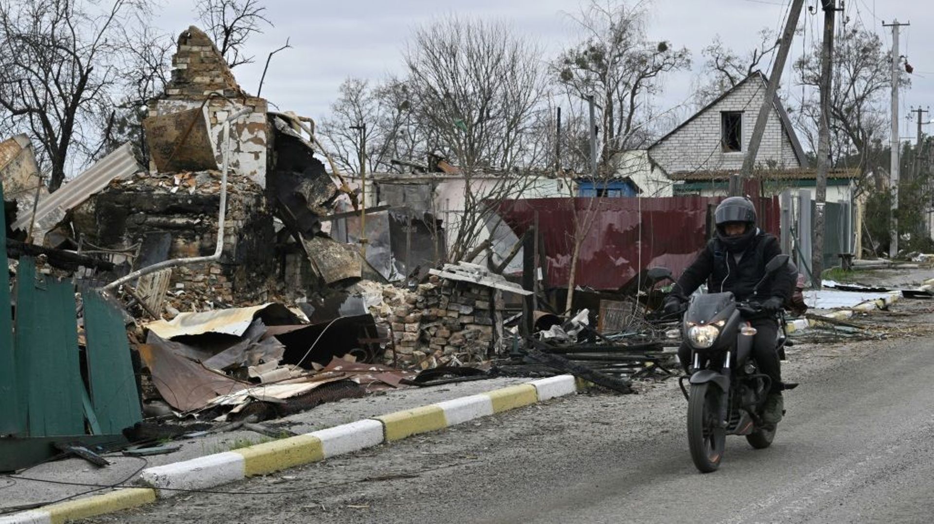 Un homme à moto passe à côté d'un bâtiment détruit dans le village de Moschchun, au nord-ouest de Kiev, le 20 avril 2022
