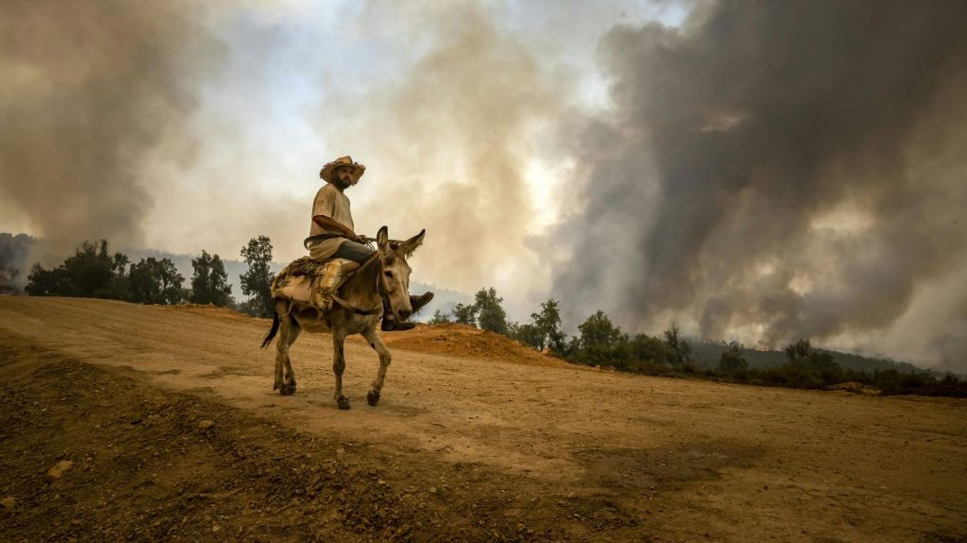 Un villageois émerge d'un nuage de fumée près de Ksar el-Kebir dans la provice marocaine de Larache, en proie à de violents incendies, le 15 juillet 2022