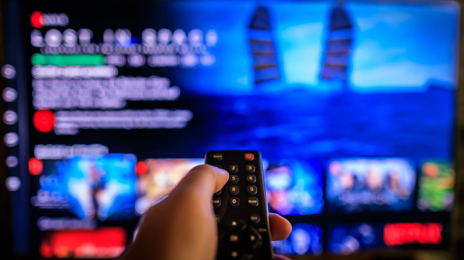 TV remote control in the foreground, Video on demand screen in the blurry background