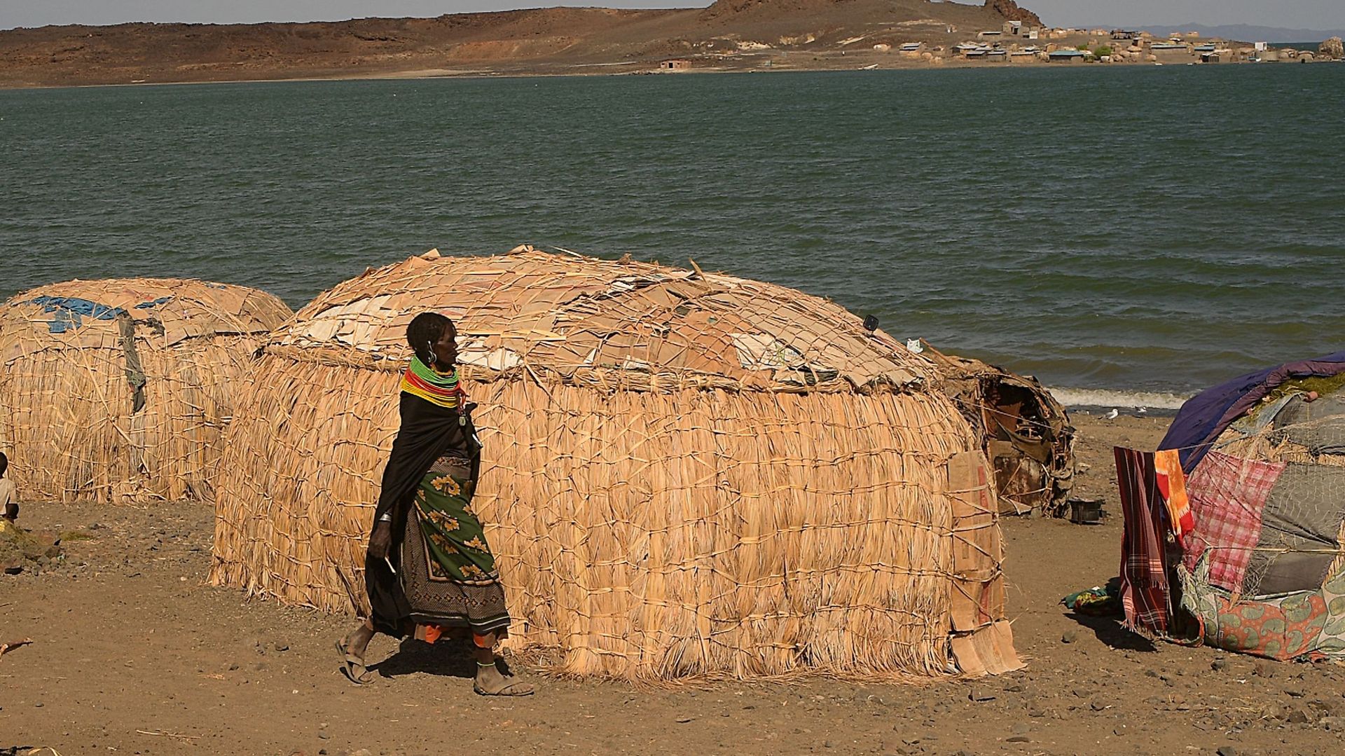 Une femme de la communauté d'El-molo passe devant de nouvelles maisons de fortune après avoir été forcée de se déplacer suite à la montée des eaux du lac Turkana, près de Loiyangalani, dans le nord du Kenya, le 13 juillet 2022.