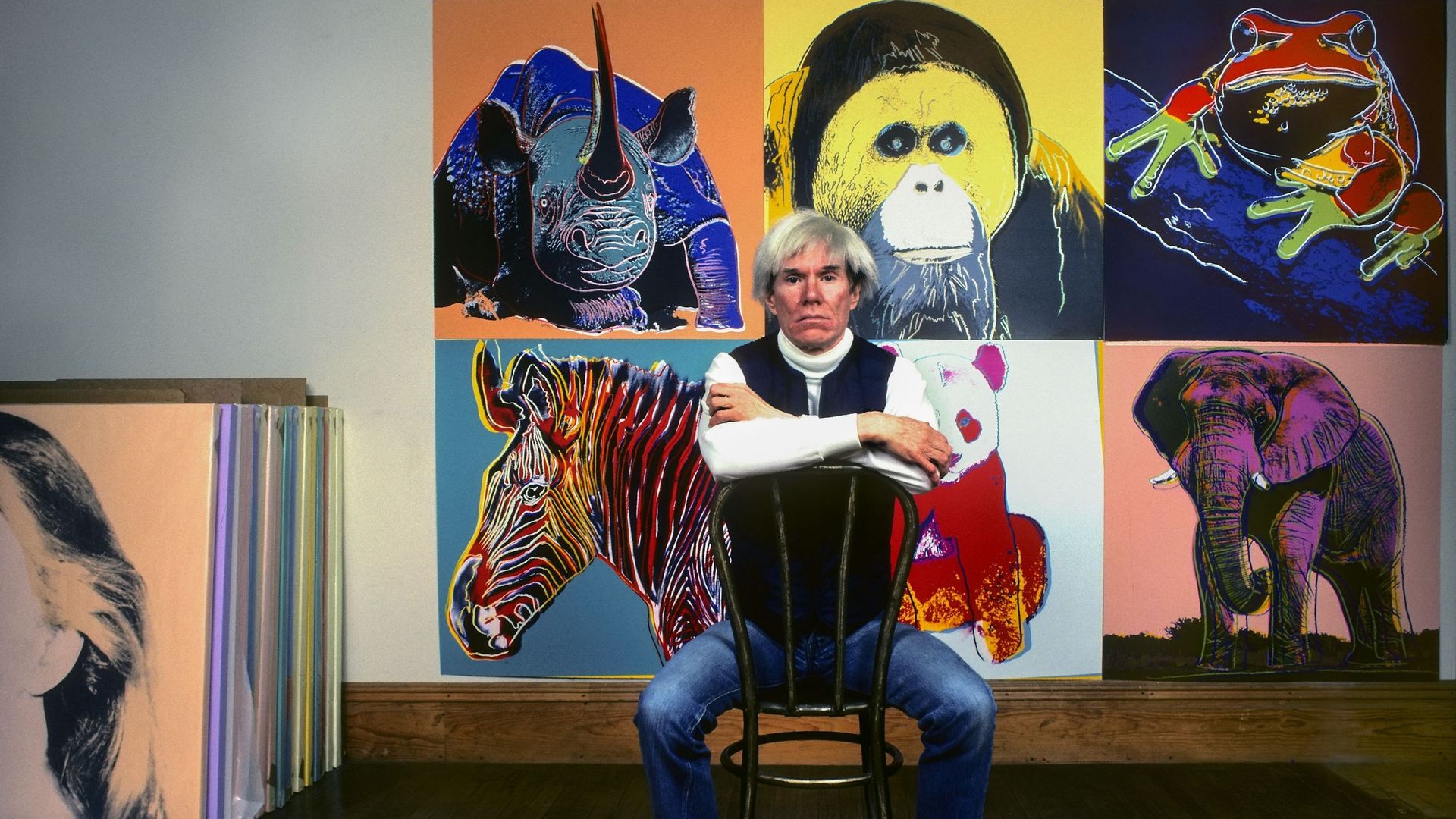 L’artiste pop américain Andy Warhol est assis devant plusieurs tableaux de son exposition "Espèces menacées" dans son studio, la Factory, à Union Square, New York, New York, le 12 avril 1983.