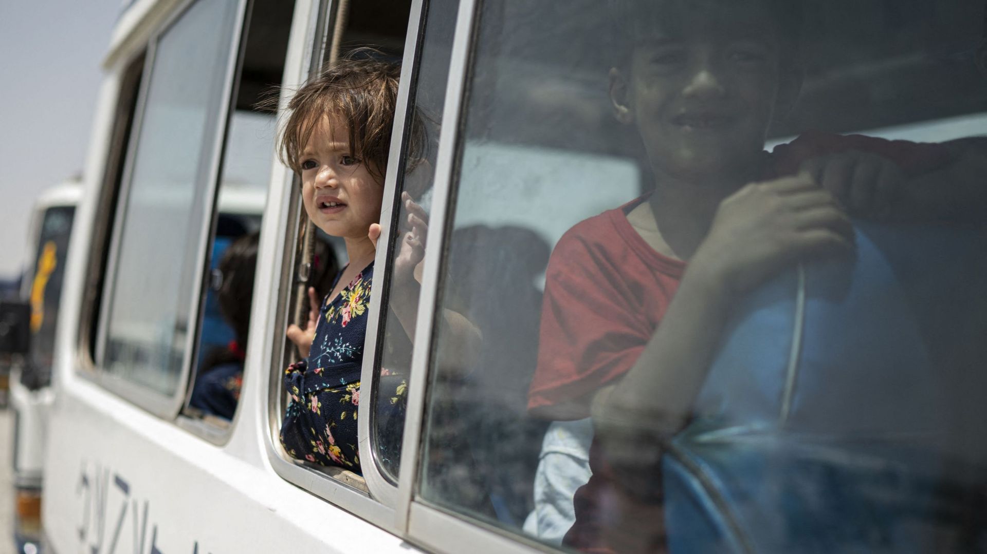 Des enfants afghans déplacés à l'intérieur du pays regardent par la fenêtre d'un bus alors qu'ils rentrent chez eux à l'est, au camp du Haut Commissariat des Nations Unies pour les réfugiés (HCR) dans la banlieue de Kaboul, le 28 juillet 2022.