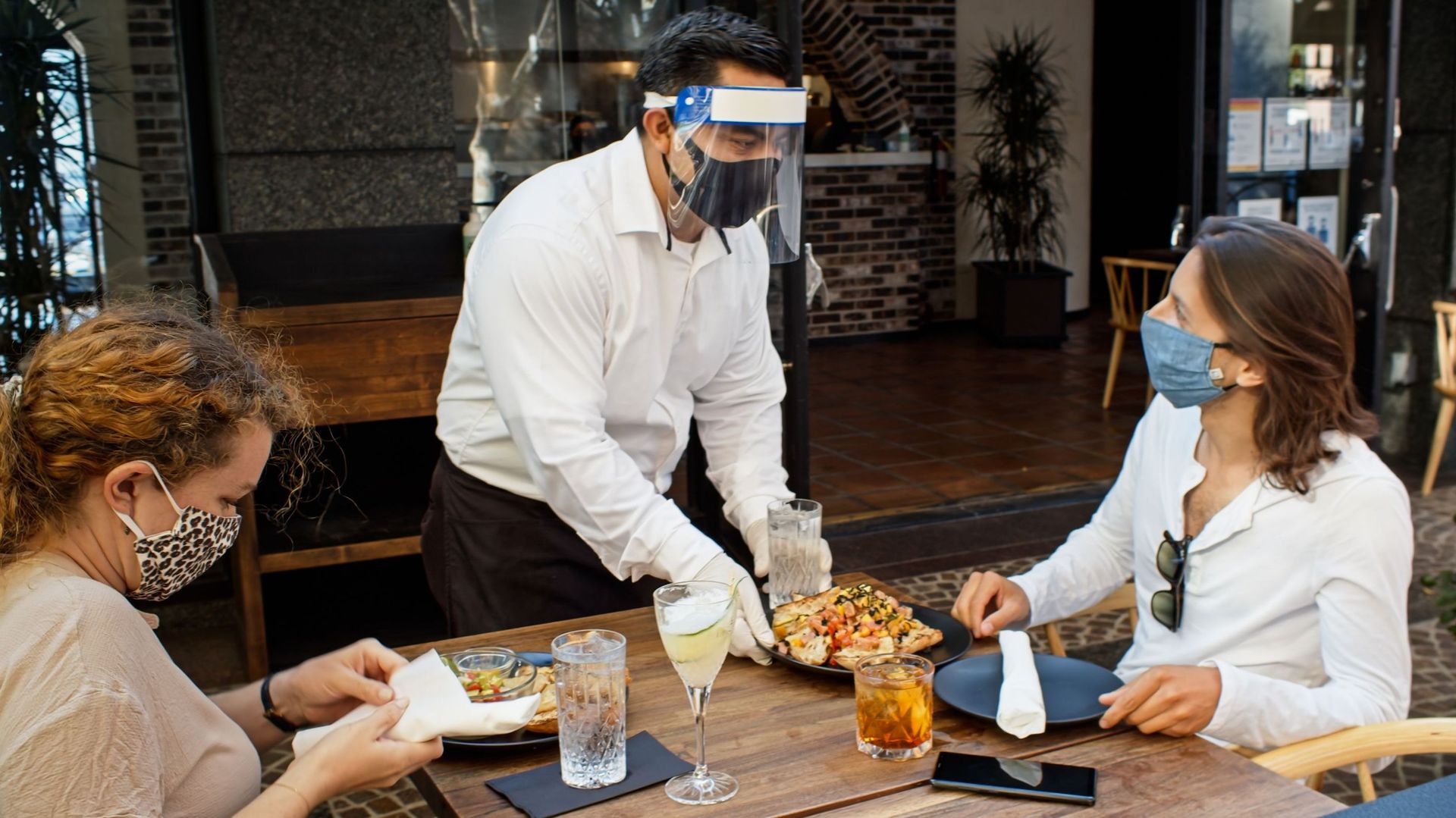 Waiter Wearing PPE During Covid-19 Pandemic Serving Food to Diners Wearing Masks
