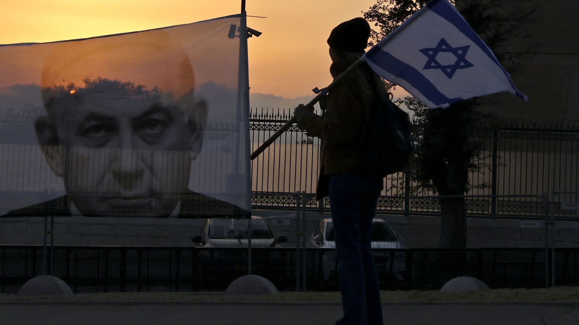 A protester walks past a banner depicting Israeli Prime Minister Benjamin Netanyahu on sunset outside the Knesset (parliament) in Jerusalem on February 20, 2023. – Demonstrators from across Israel descended on Jerusalem to rally near parliament ahead of t