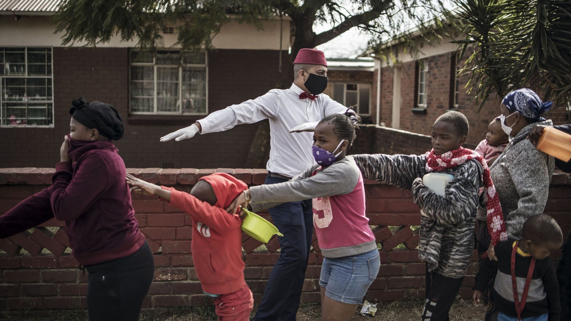 Un bénévole et les enfants qui font la queue pour maintenir la distance sociale à Johannesburg en Afrique du Sud, le 25 mai 2020, lors d'un repas de l'Aïd al-Fitr distribué à des centaines de bénéficiaires dans les quartiers de Westbury et de Coronationvi