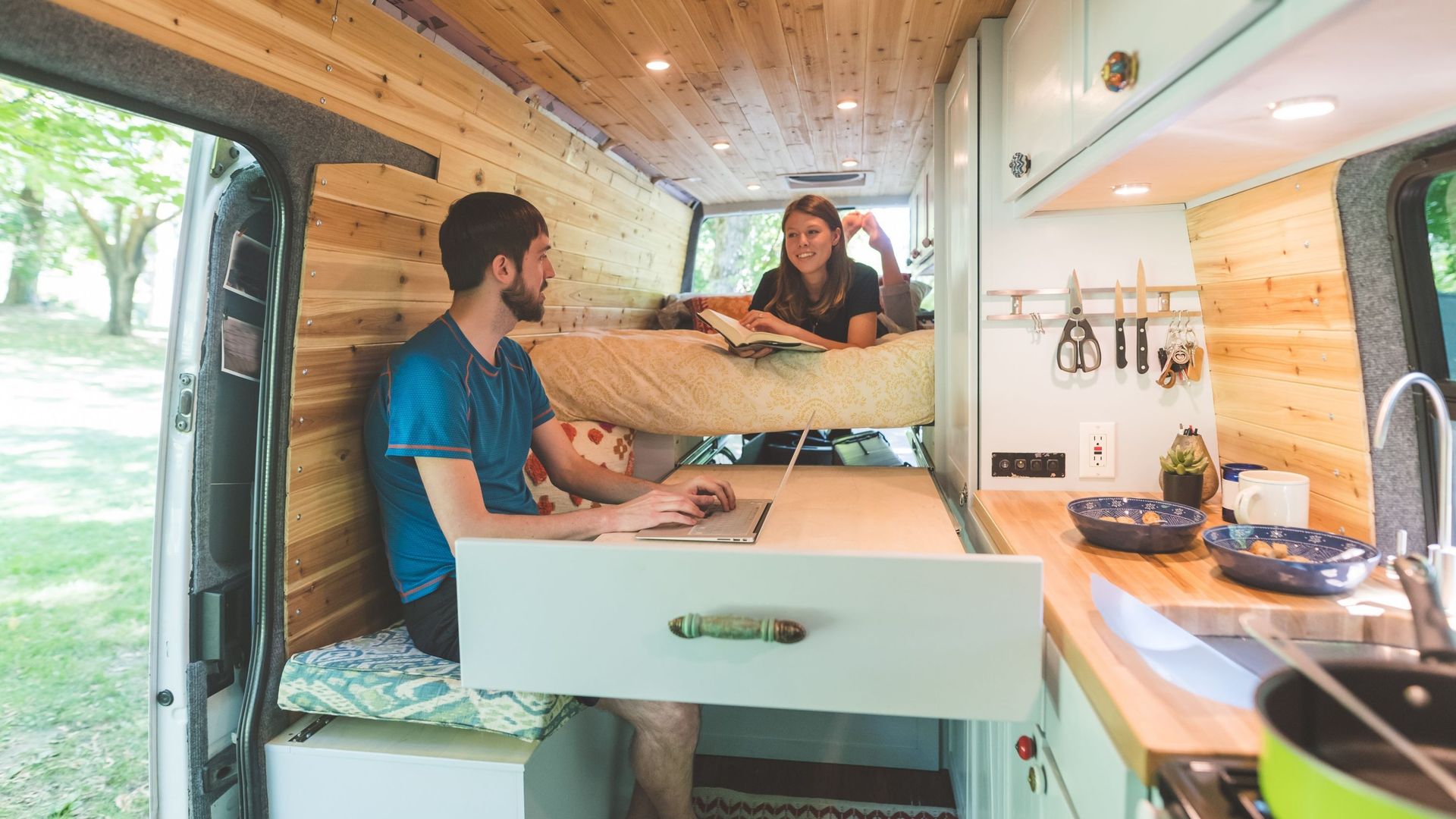 Vue intérieure d’un van aménagé où l’espace est optimisé en espace bureau, couchage et cuisine