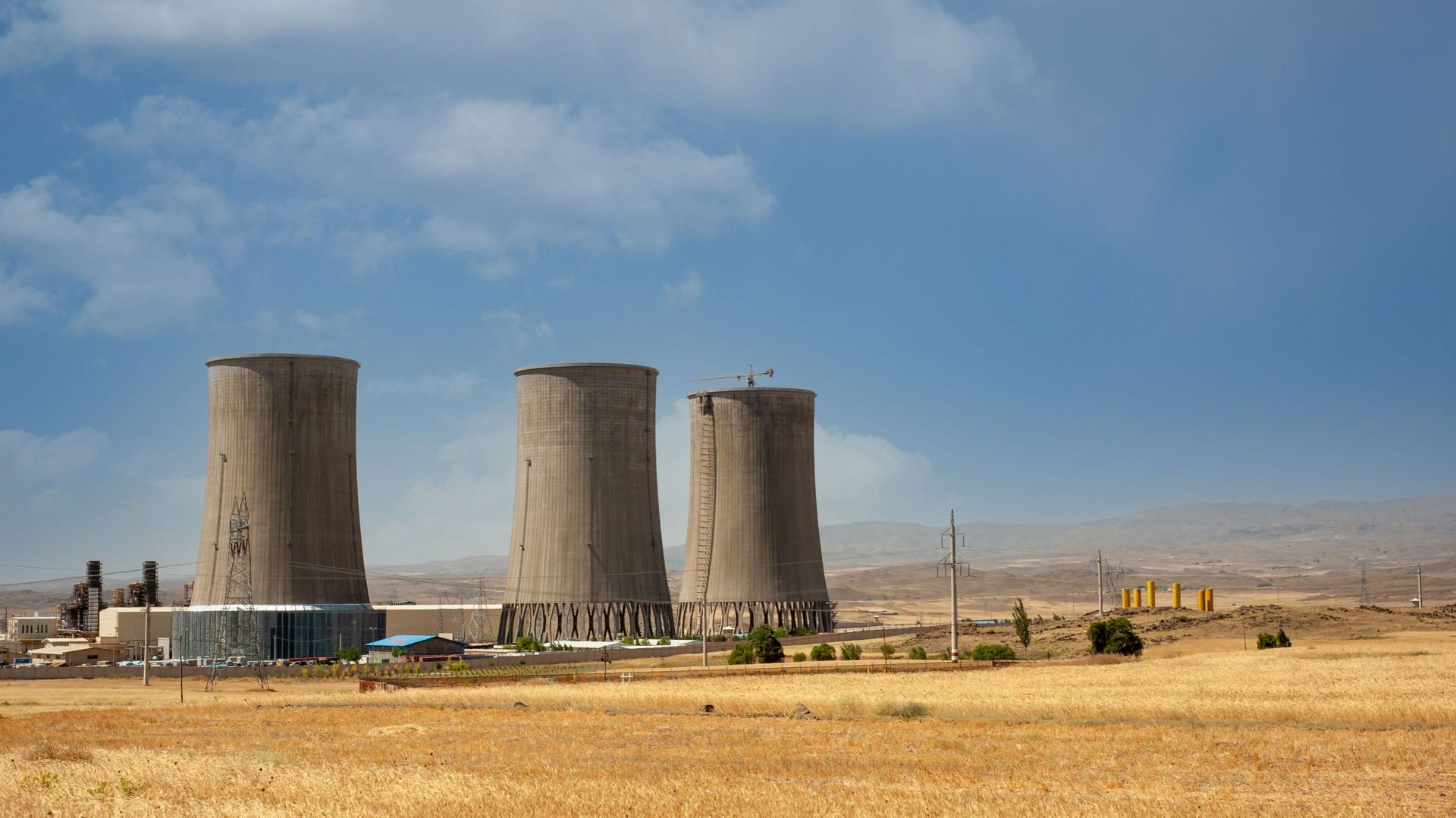 Image d'illustration - Tours de refroidissement de centrales nucléaires, grandes cheminées à côté du champ de blé avec un ciel partiellement nuageux dans la province du Kurdistan, Iran.