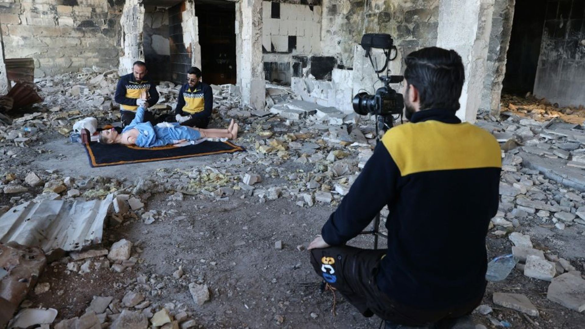 Face à une caméra, des secouristes des Casques blancs à Ariha en Syrie utilisent un mannequin allongé au sol pour montrer comment traiter un blessé dans la guerre, une vidéo destinée aux secouristes ukrainiens, le 16 mars 2022