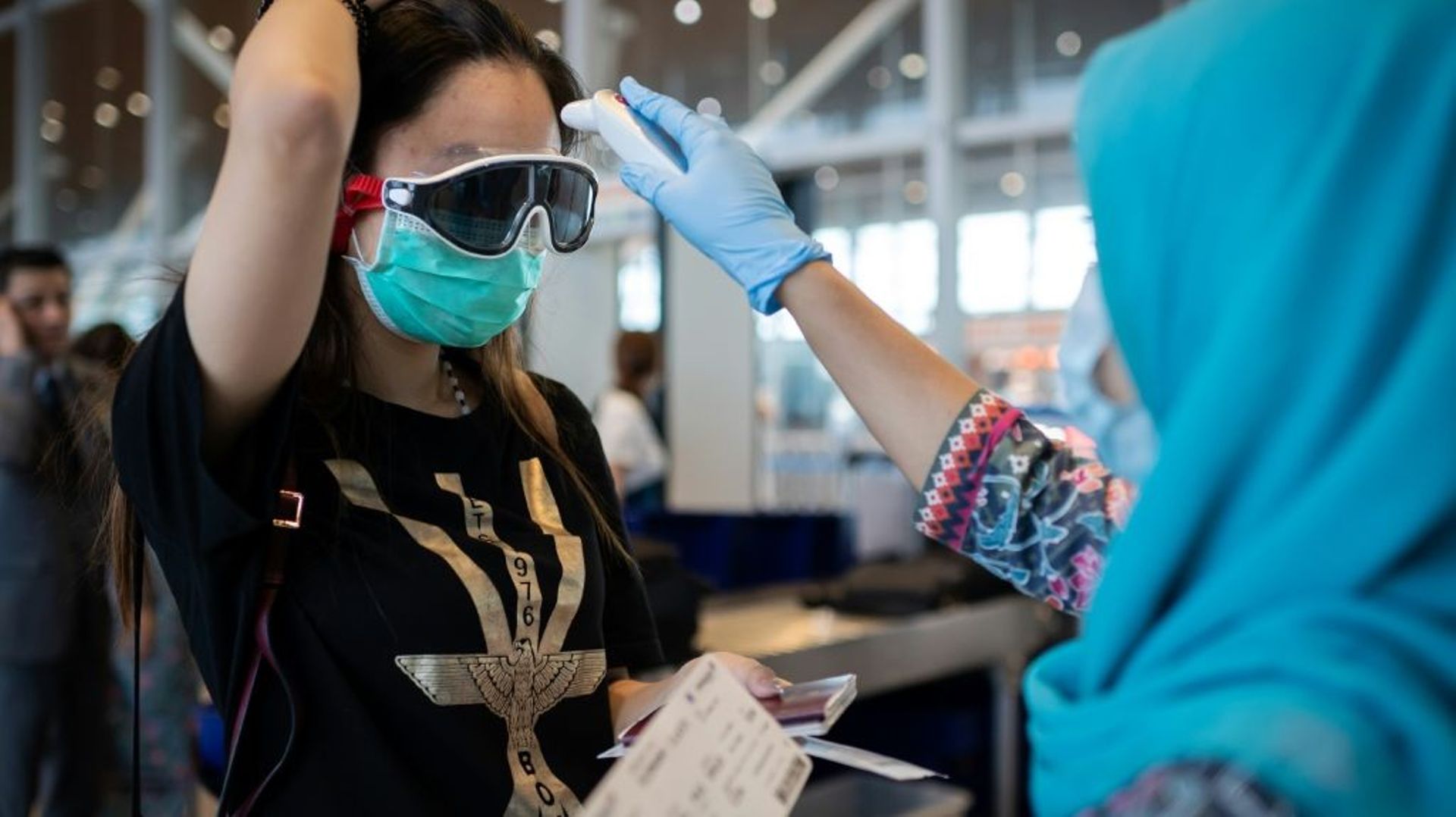 Une hôtesse de l'air de Malaysia Airlines prend la température d'une passagère chinoise à l'embarquement d'un vol pour Pékin, le 14 février 2020 à l'aéroport de Kuala Lumpur