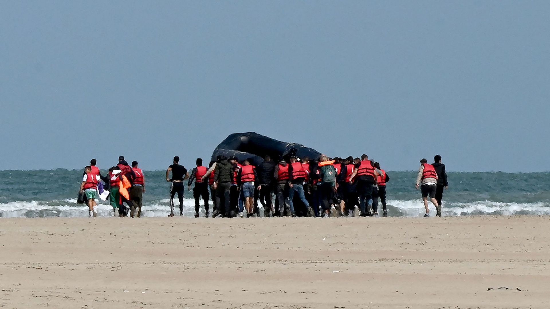 Image d'illustration : des migrants poussent un bateau pneumatique sur une étendue de sable en direction de l'eau, près de Gravelines, dans le nord de la France, le 25 août 2022, avant de tenter de traverser la Manche vers la Grande-Bretagne.
