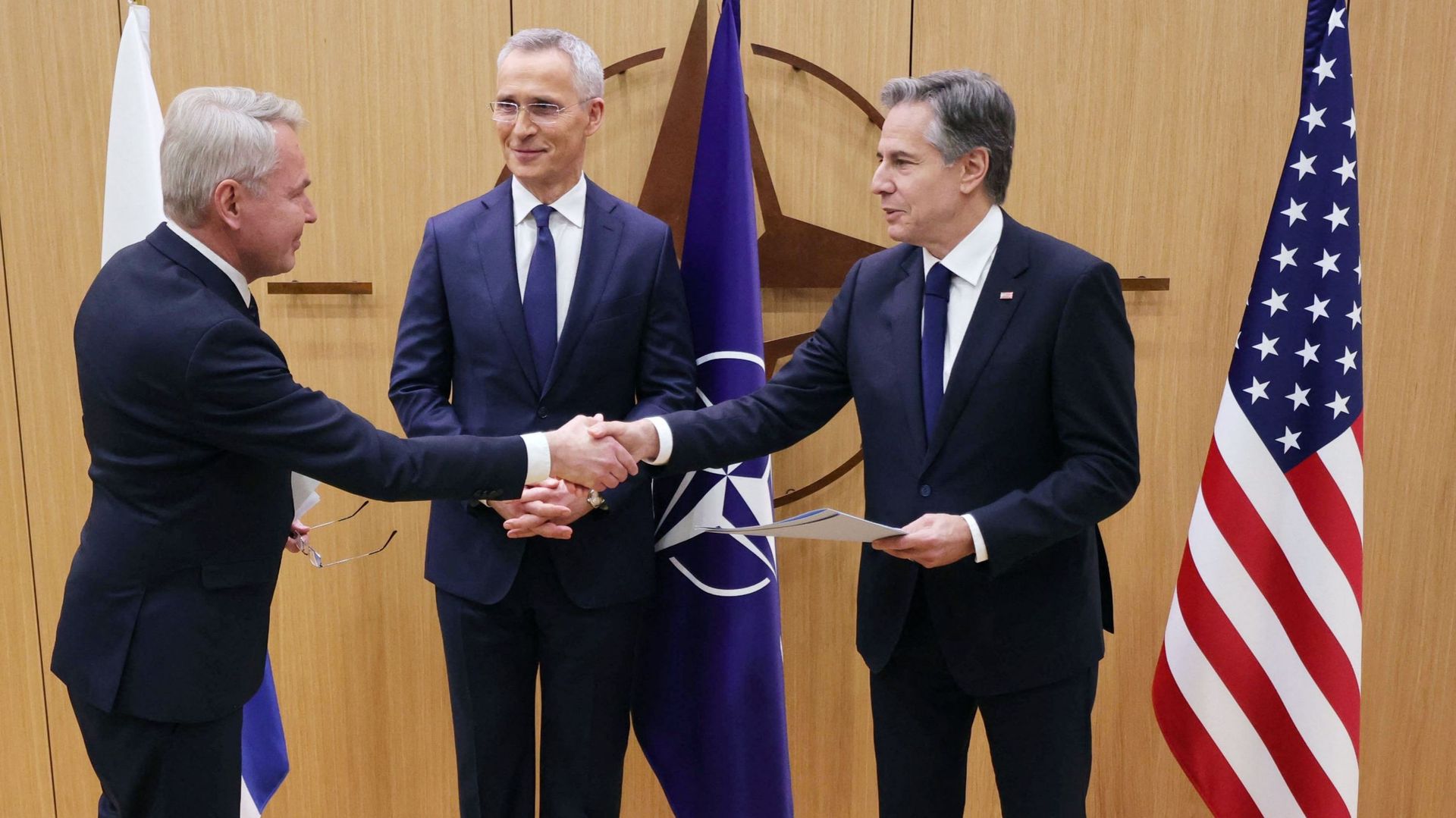 Le ministre finlandais des Affaires étrangères Pekka Haavisto (G) serre la main du secrétaire d'État américain Antony Blinken, entouré du secrétaire général de l'OTAN Jens Stoltenberg (C) qui lui remet les documents d'adhésion de la Finlande à l'OTAN.