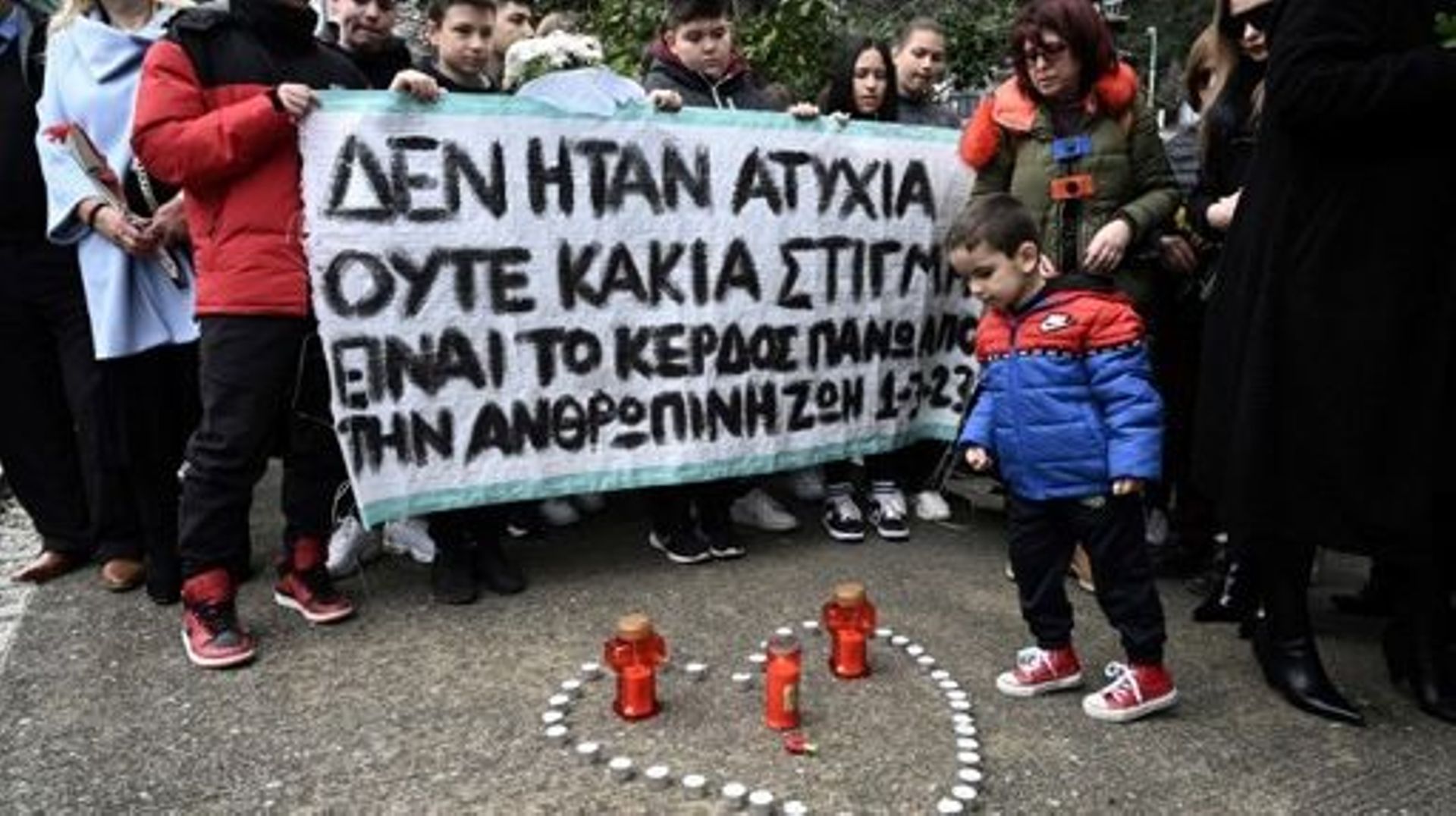 Members of the public hold a banner reading "I was not an accident or bad timing, it is the money above human life" at the railway station of Rapsani, north Greece, on March 5, 2023, during a commemorative gathering for the victims of a deadly train crash
