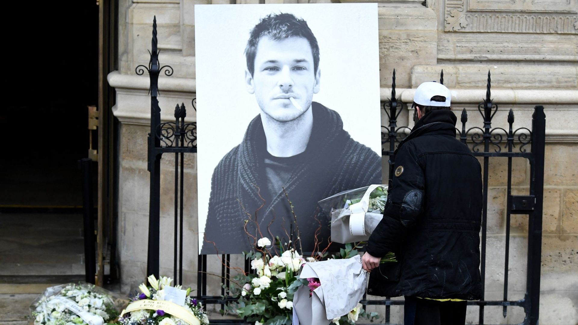 Un homme dépose des fleurs près d’un portrait de l’acteur français Gaspard Ulliel devant l’église Saint-Eustache à Paris, le 27 janvier 2022, en prévision de ses funérailles après sa mort à 37 ans à la suite d’un accident de ski le 19 janvier 2022.