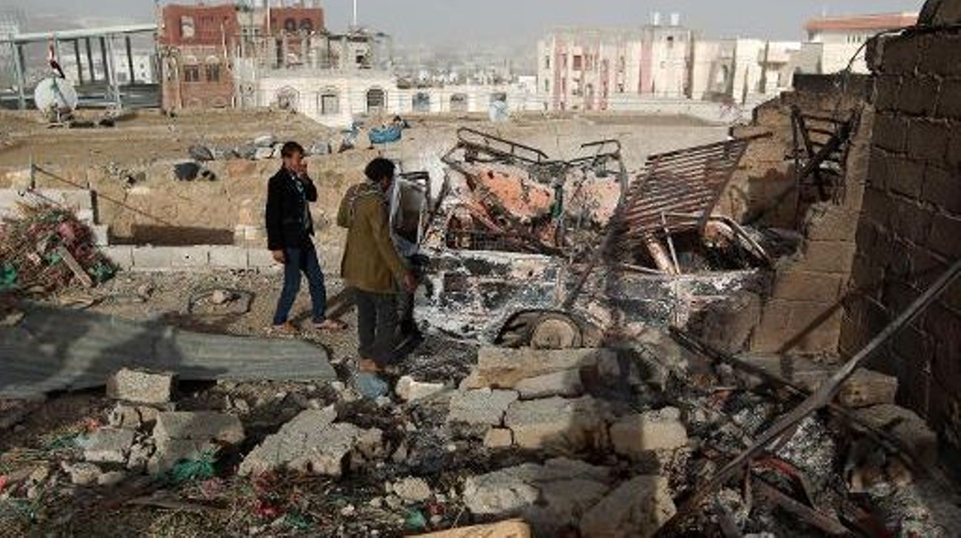 Des Yéménites près d'un véhicule et d'un bâtiment détruits près du palais présidentiel, le 20 janvier 2015 à Sanaa