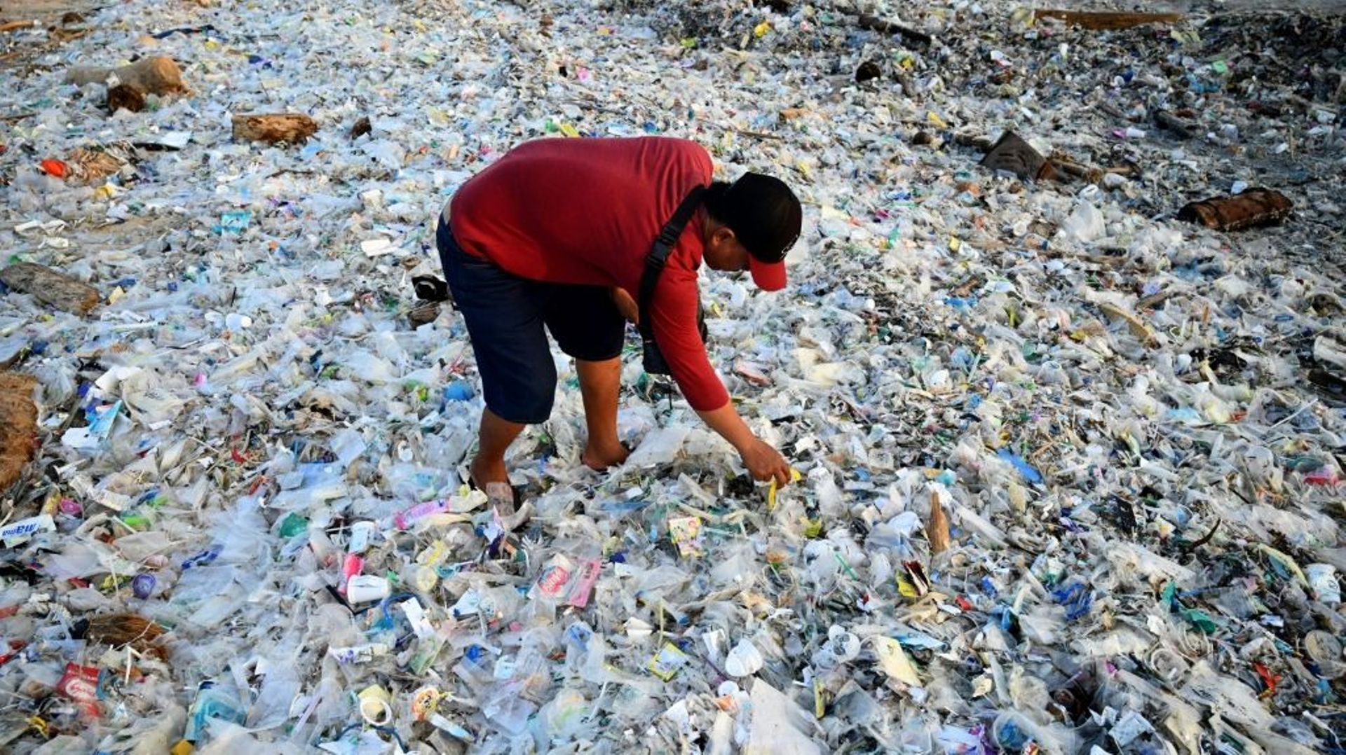 Un homme fouille dans des ordures et déchets plastiques échoués sur la plage de Kedonganan, sur l’île indonésienne de Bali, le 19 mars 2024.